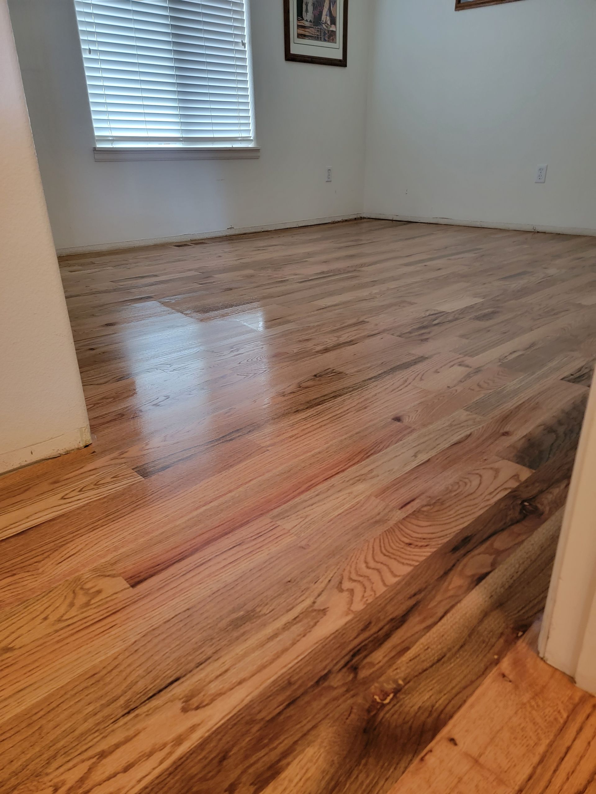 Empty room with glossy hardwood floors and a window with blinds