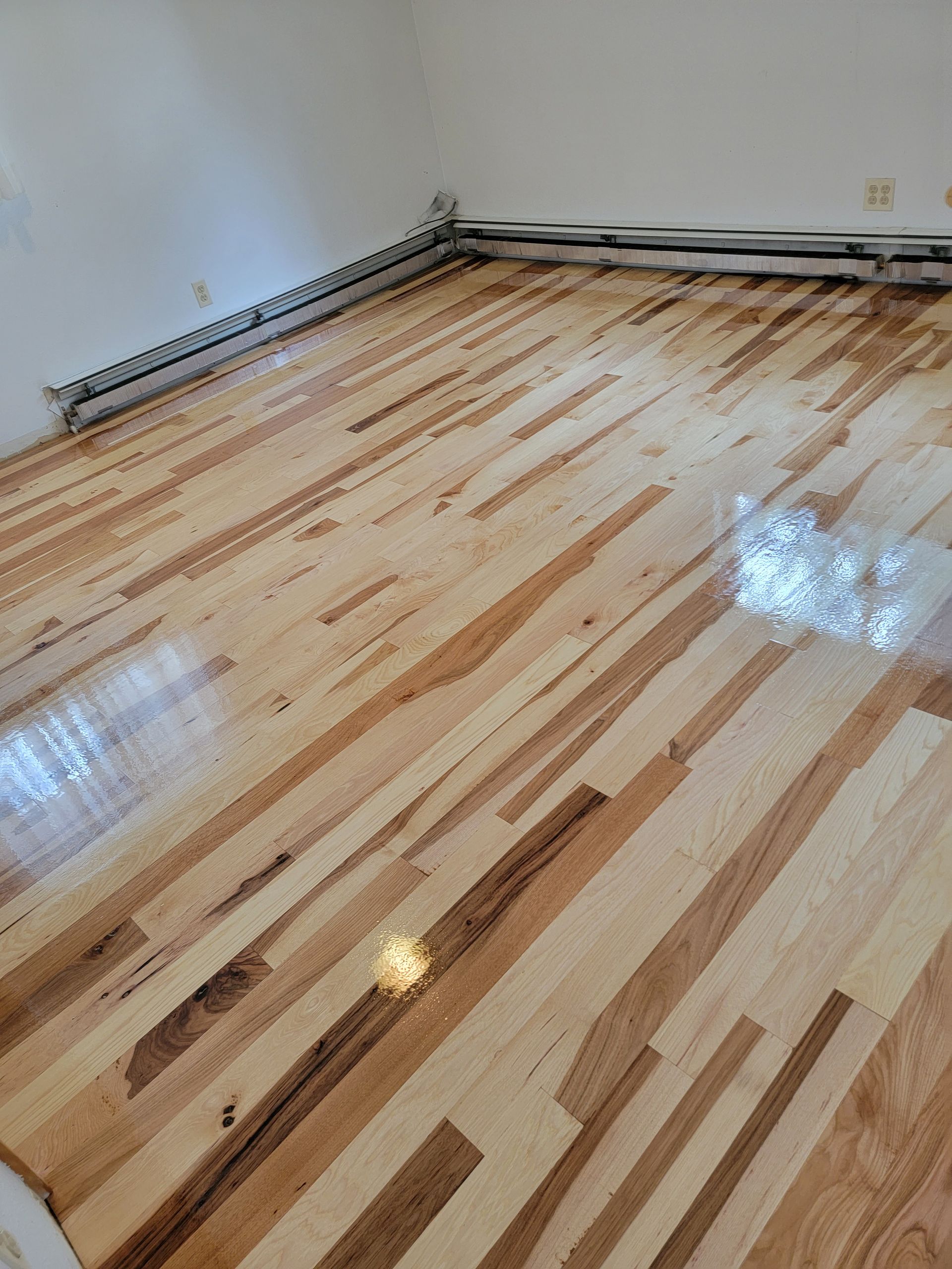 Empty room with glossy striped hardwood floor and baseboard heaters along the walls
