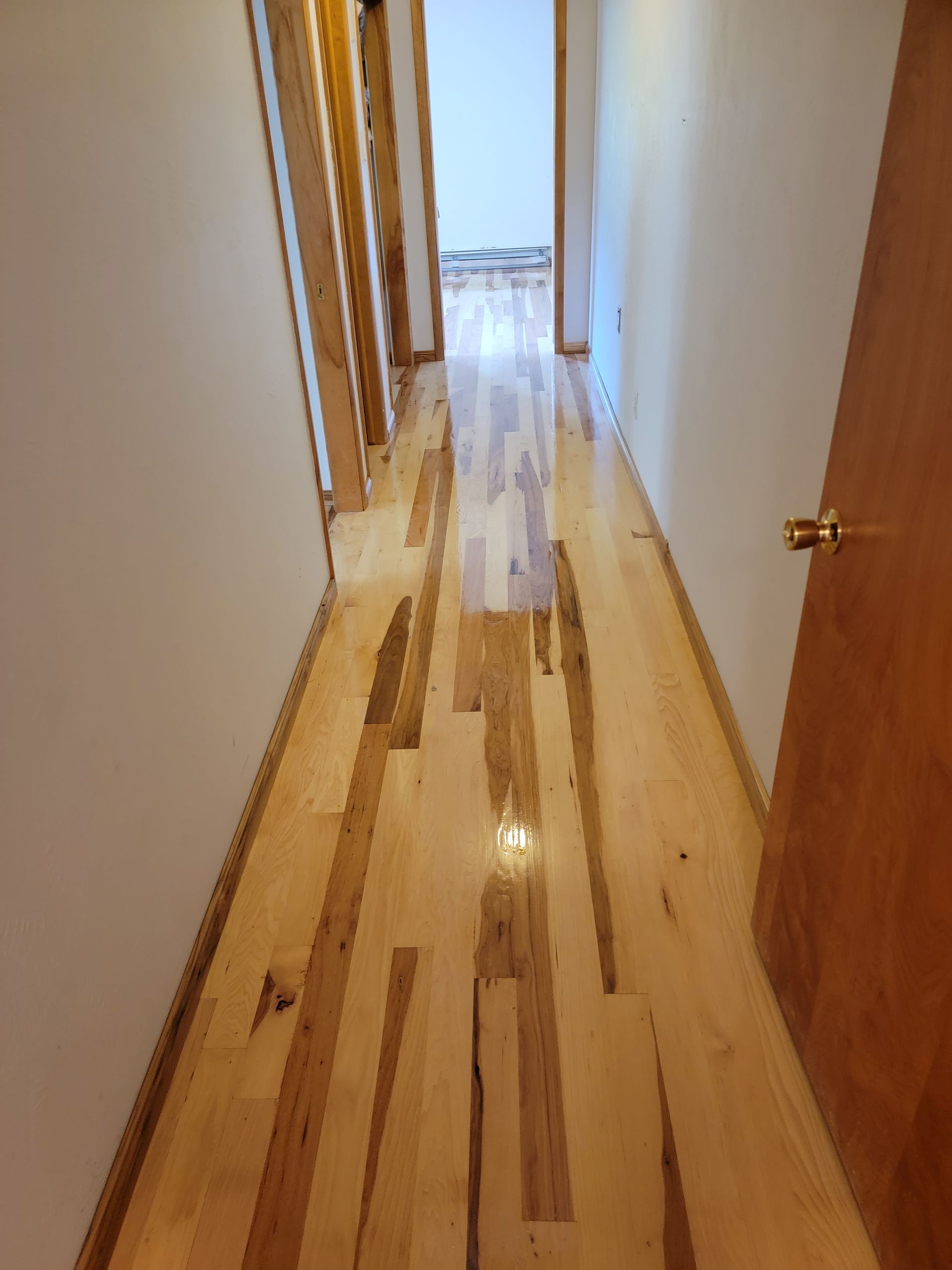 Narrow hallway with wood floors, white walls, and an open door at the end.