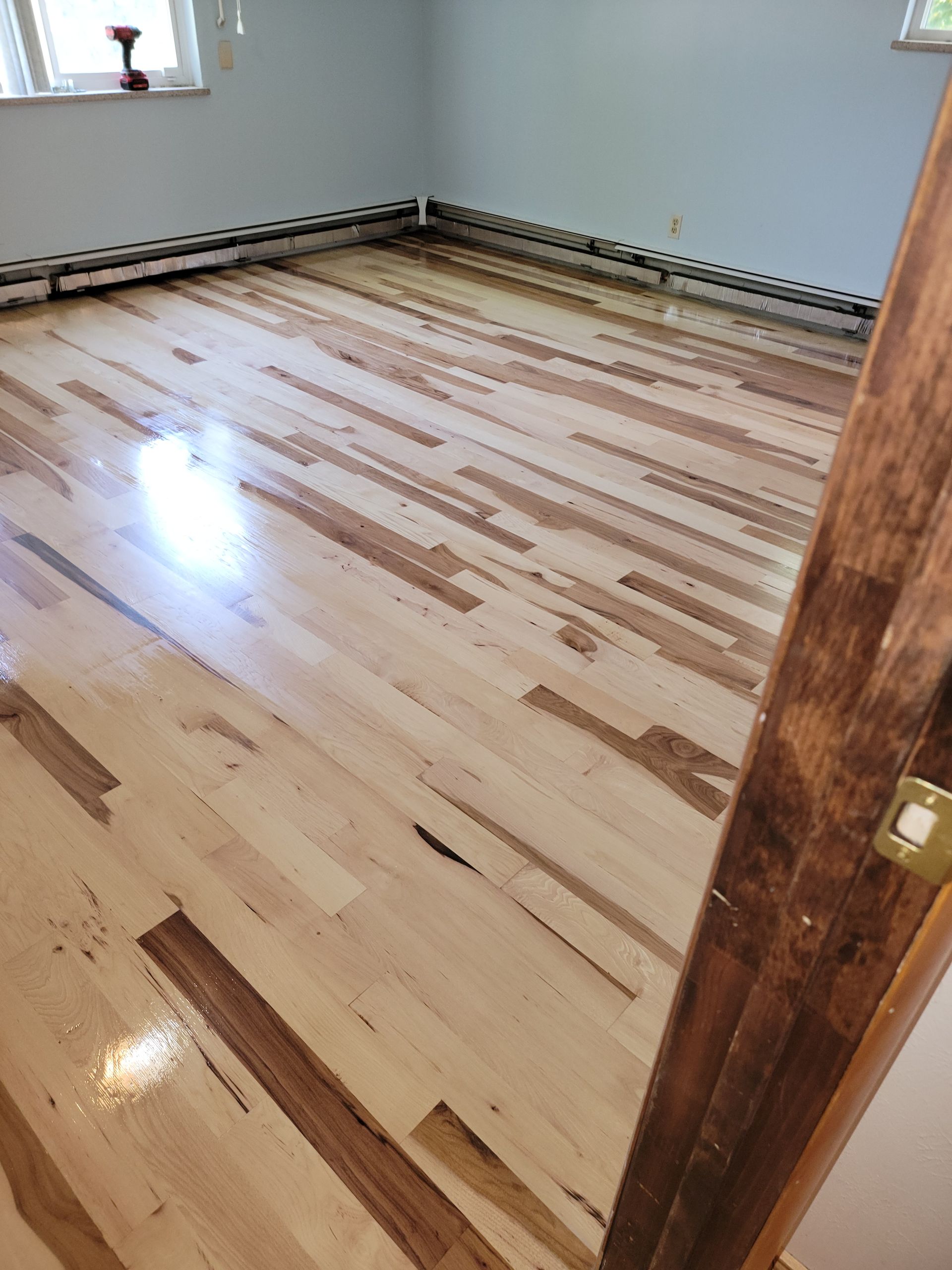 Empty room with newly refinished hardwood floor and light-colored walls