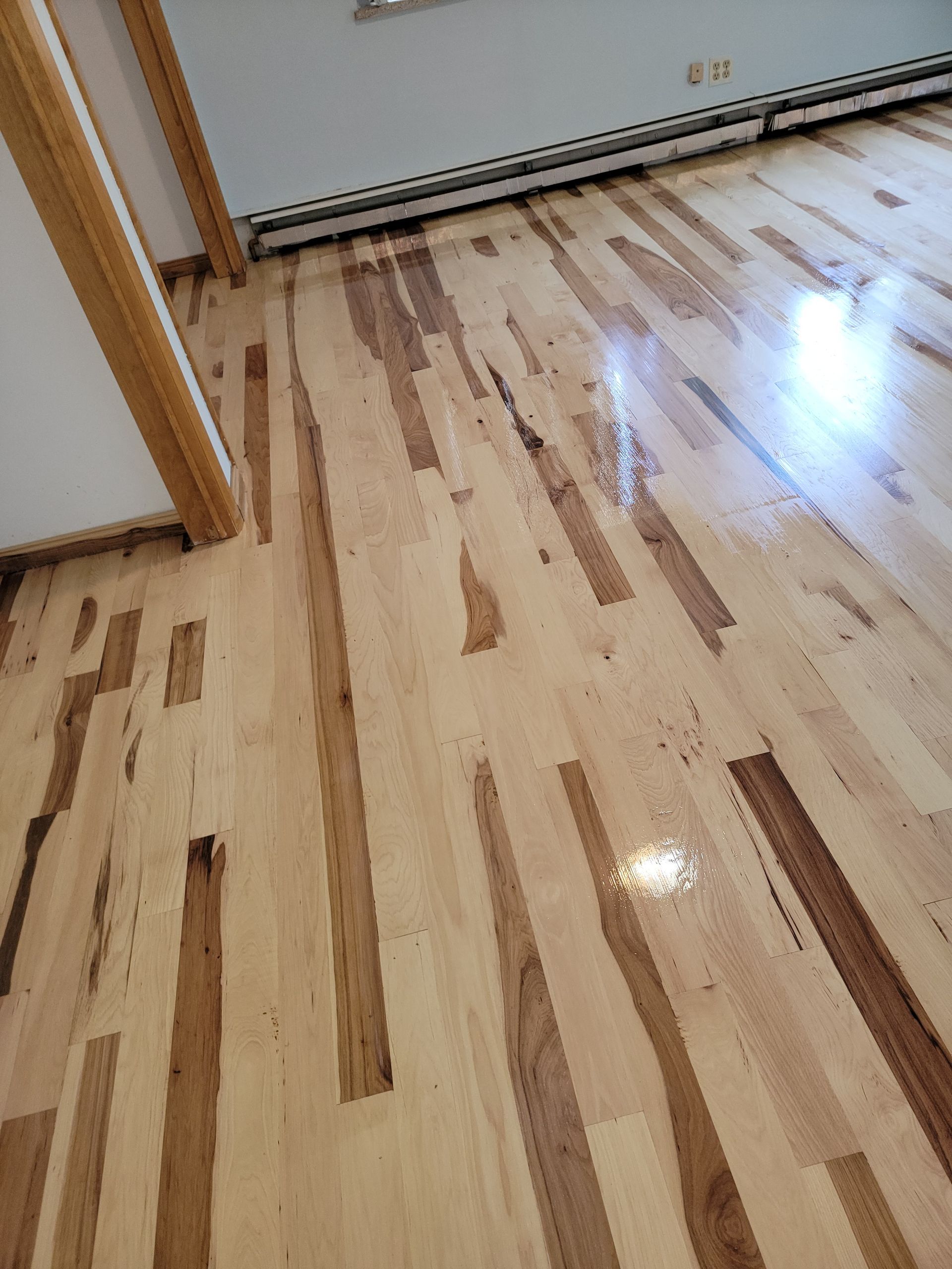 Glossy hardwood floor with light and dark wood planks near a doorway and baseboard radiator