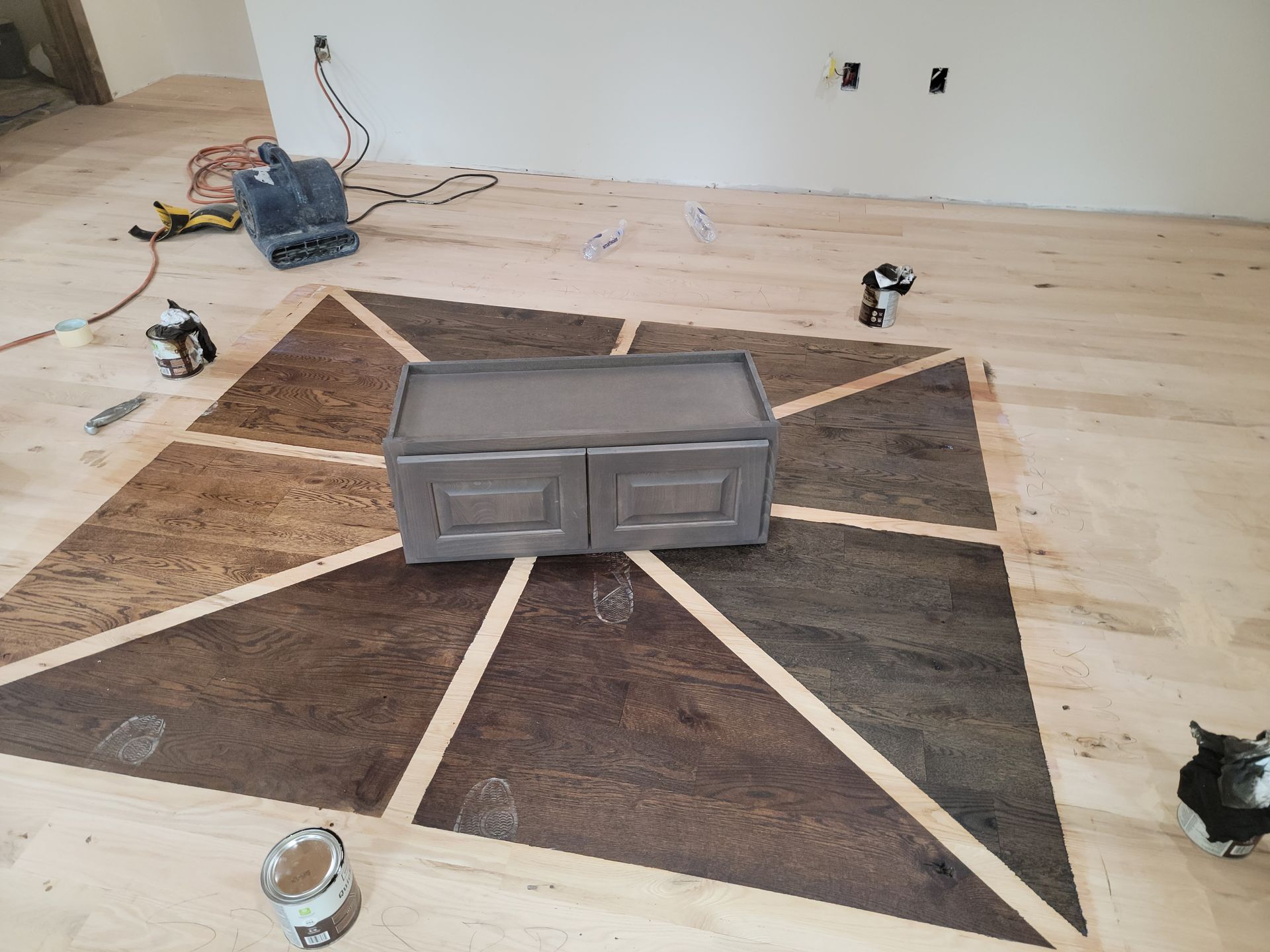 Living room with a large geometric rug and a gray cabinet centered on a light wood floor.