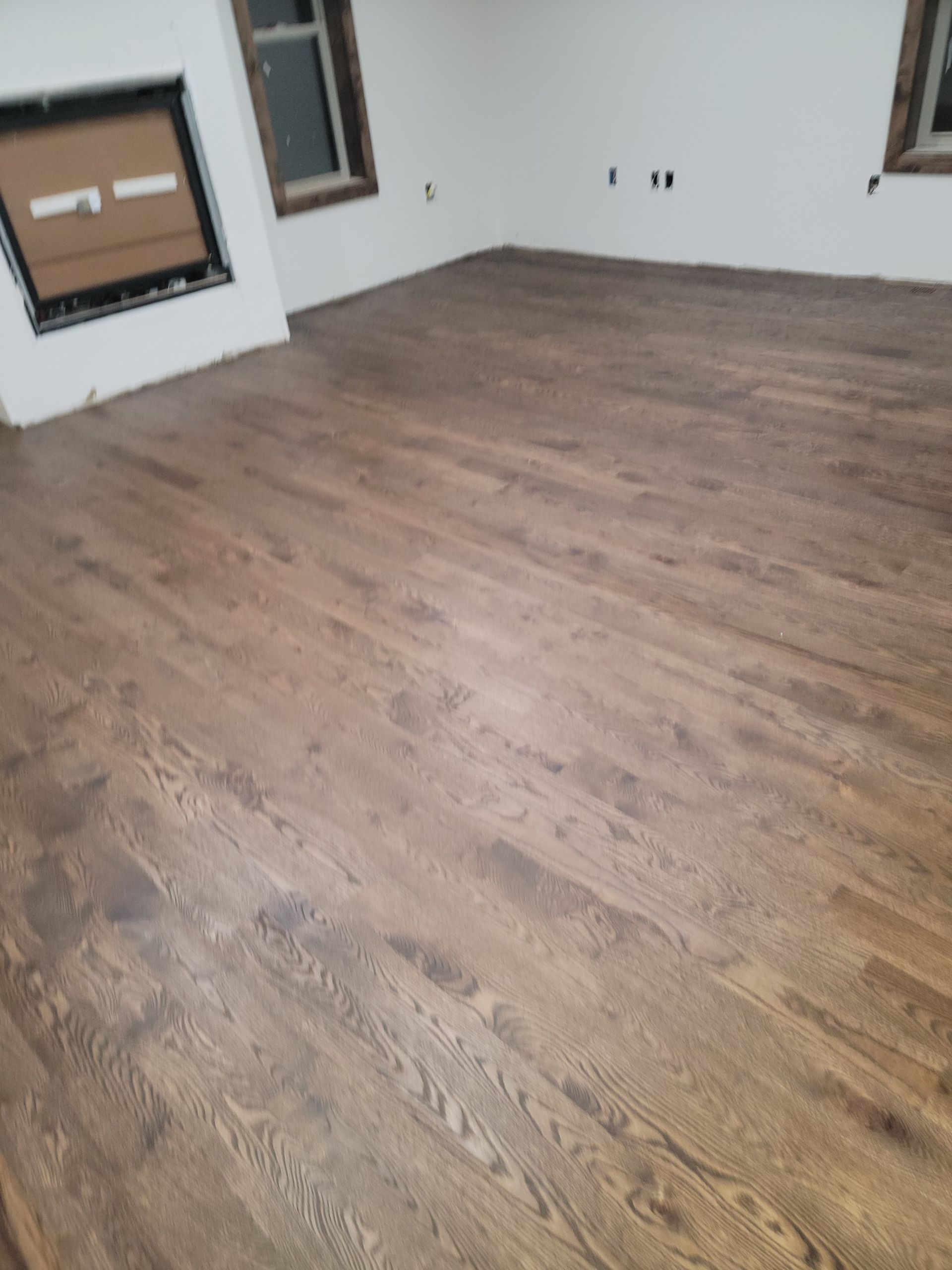 Empty room with brown wood flooring, white walls, and windows on two sides