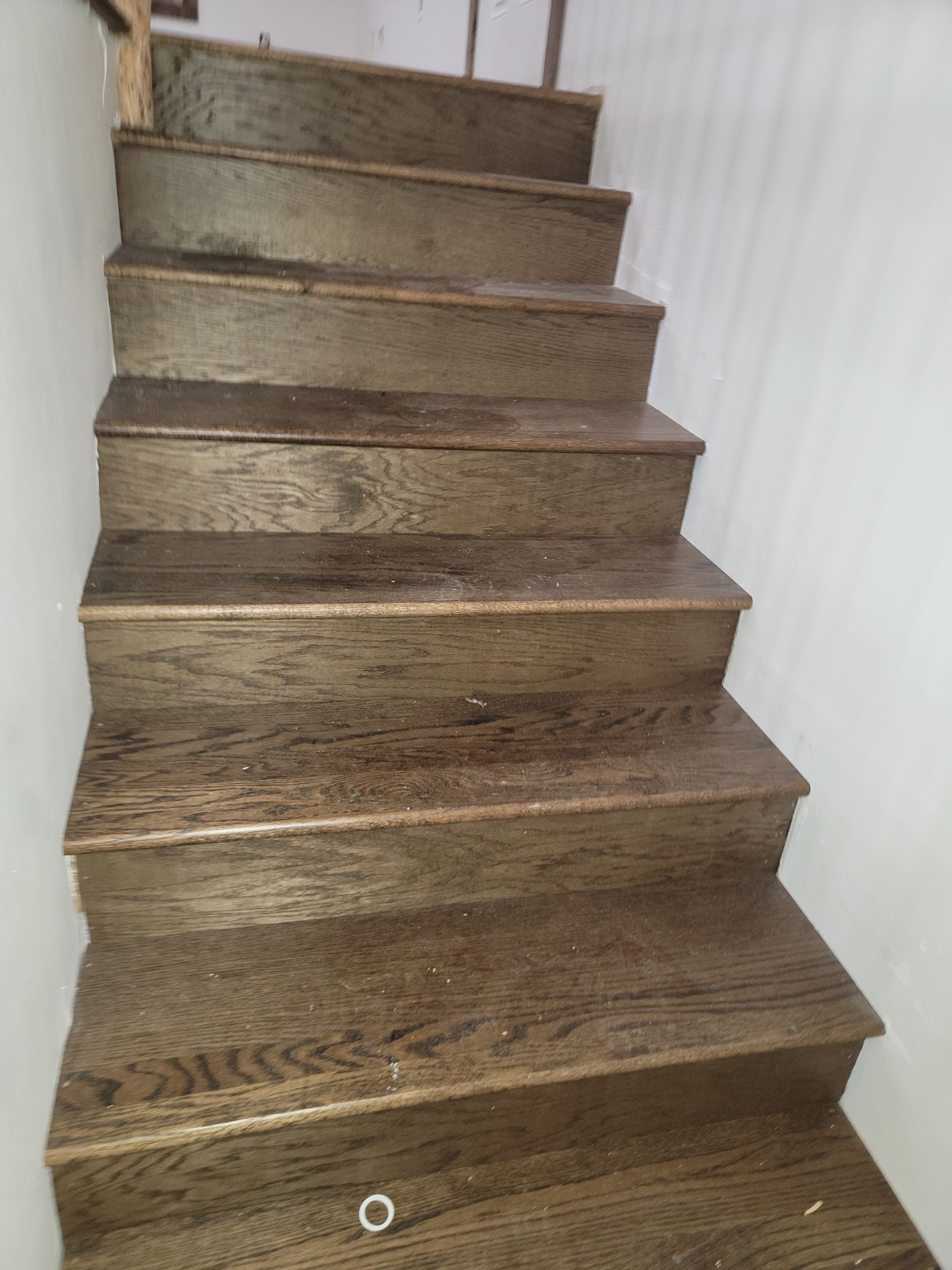 Narrow carpeted staircase with brown wooden treads and a white wall on the right