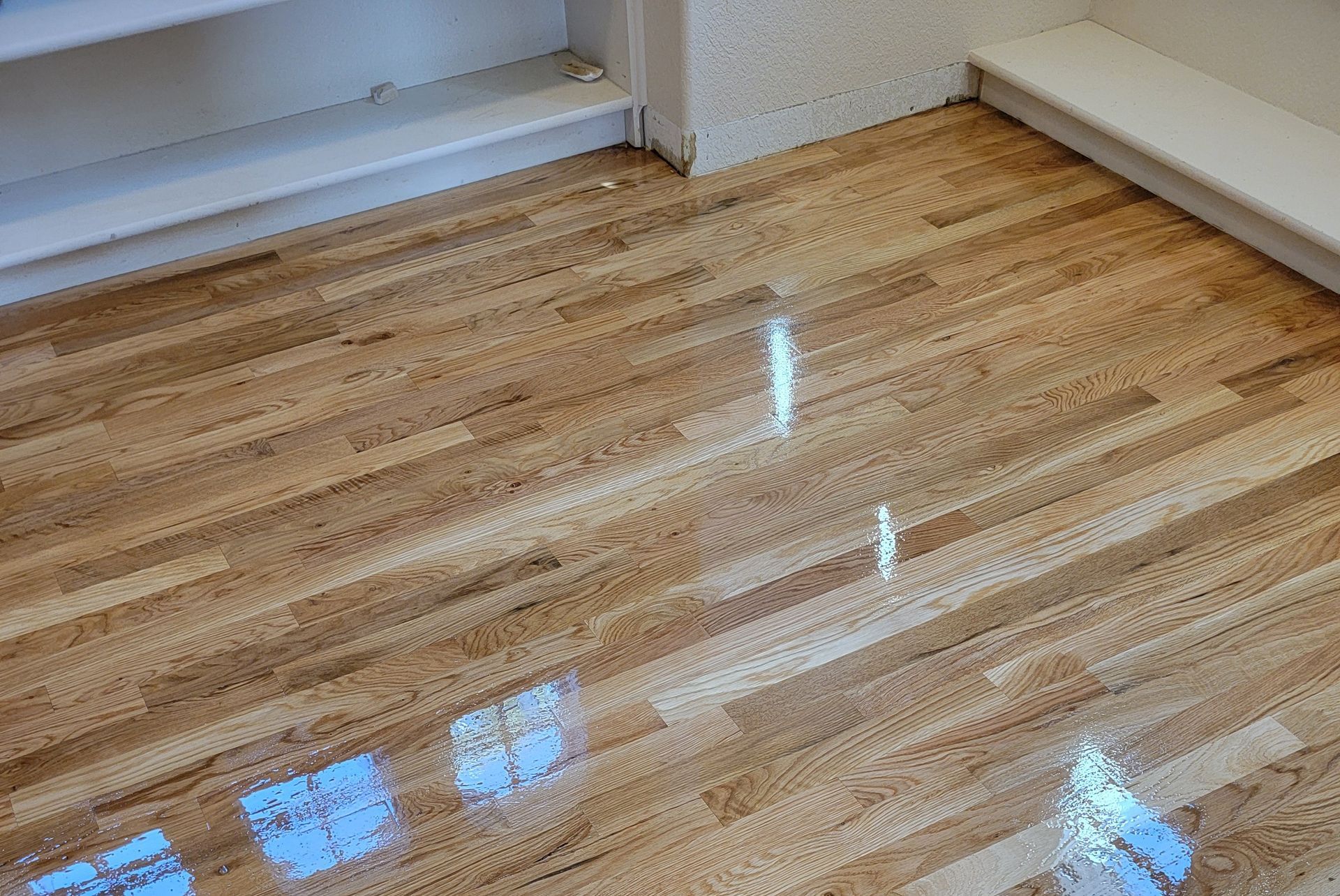 Shiny hardwood floor in an empty room with white walls and built-in shelves.