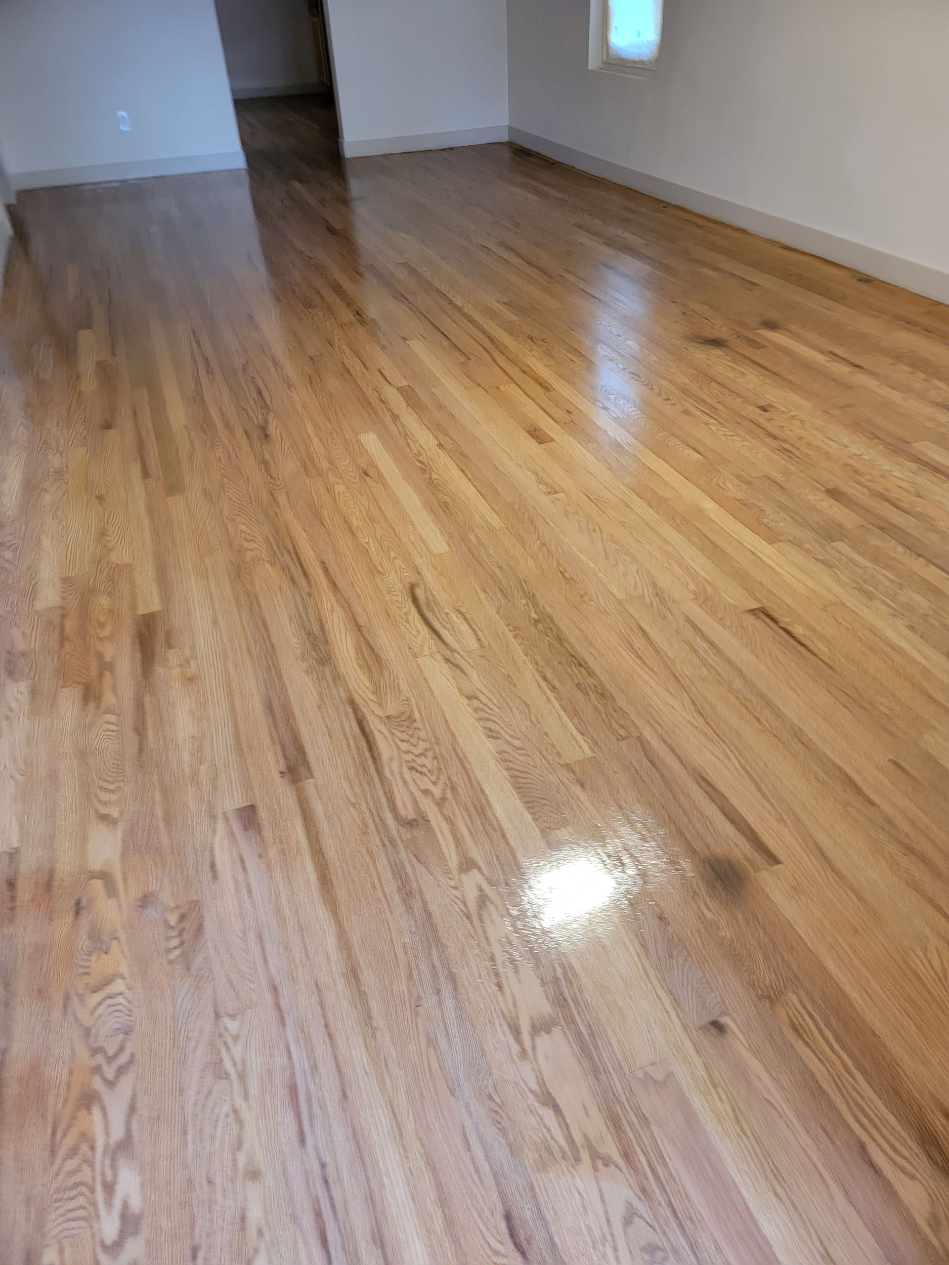 Shiny hardwood floor in an empty room with white walls and a window reflection
