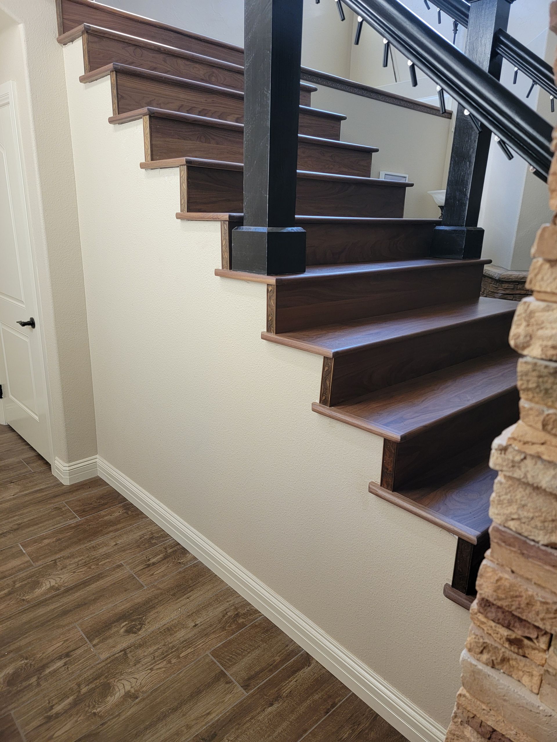 Staircase with dark wood steps, black railing, and beige walls above wood flooring