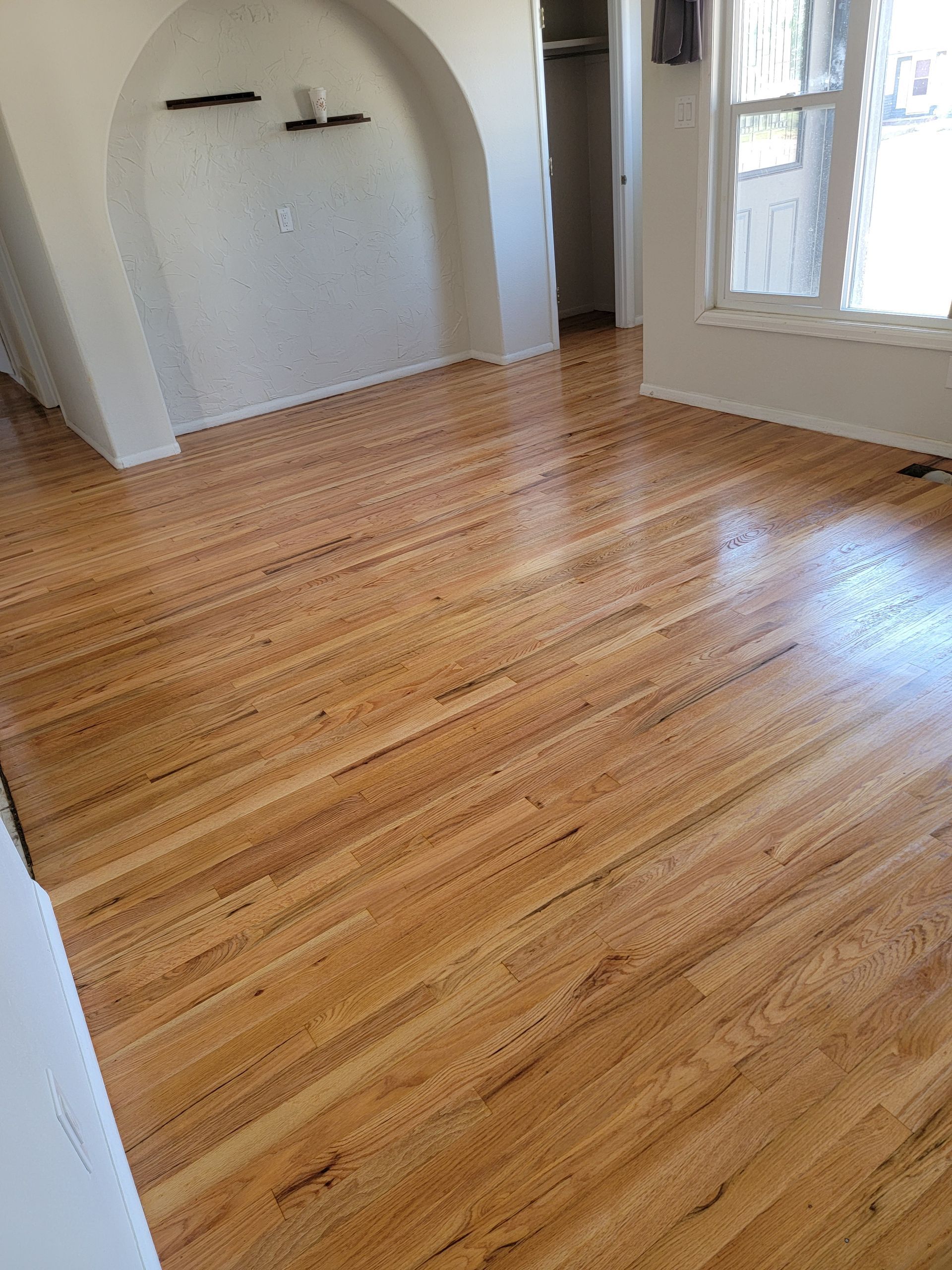 Empty room with polished hardwood floor, arched alcove, and large window with white trim