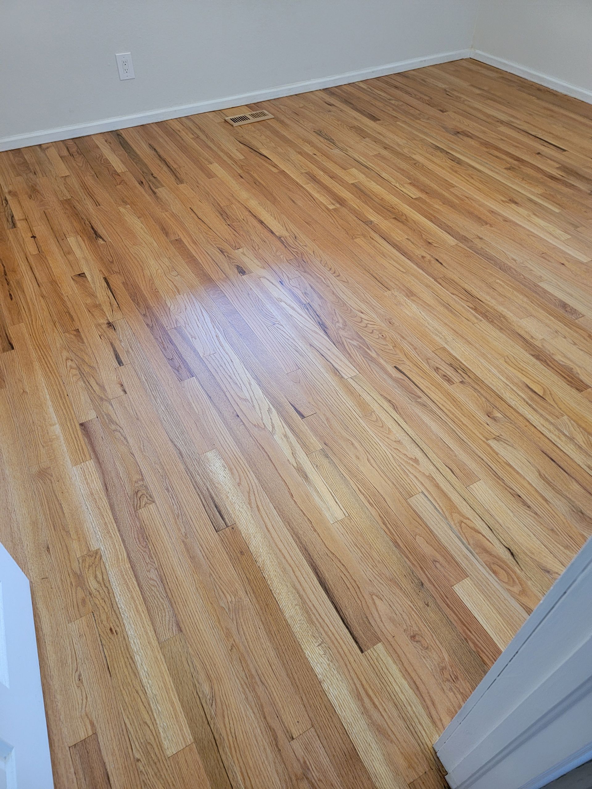 Empty room with light hardwood floor and white walls, seen from a doorway