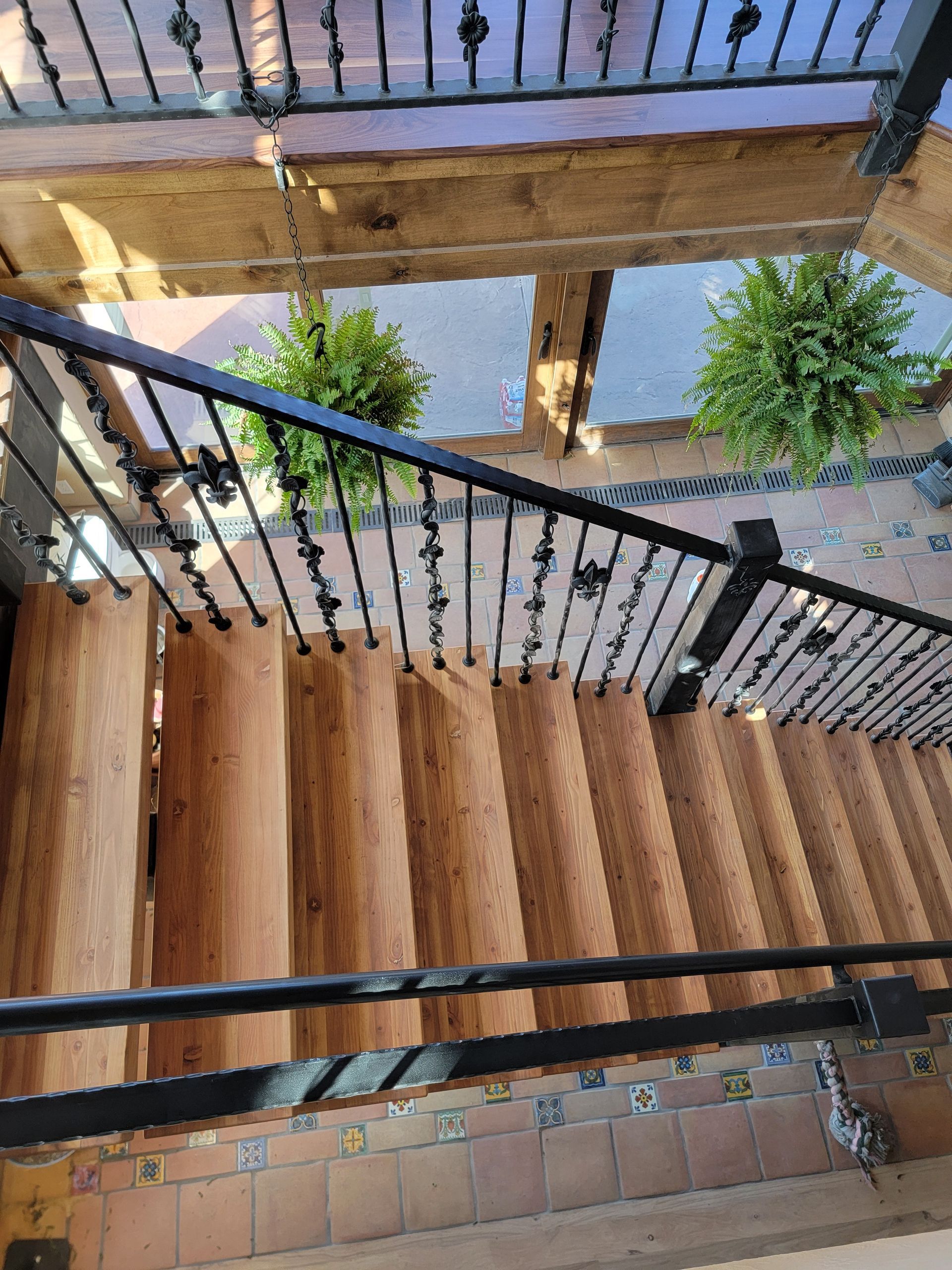 Staircase with black wrought-iron railings and wooden steps beside a courtyard with potted plants and water below