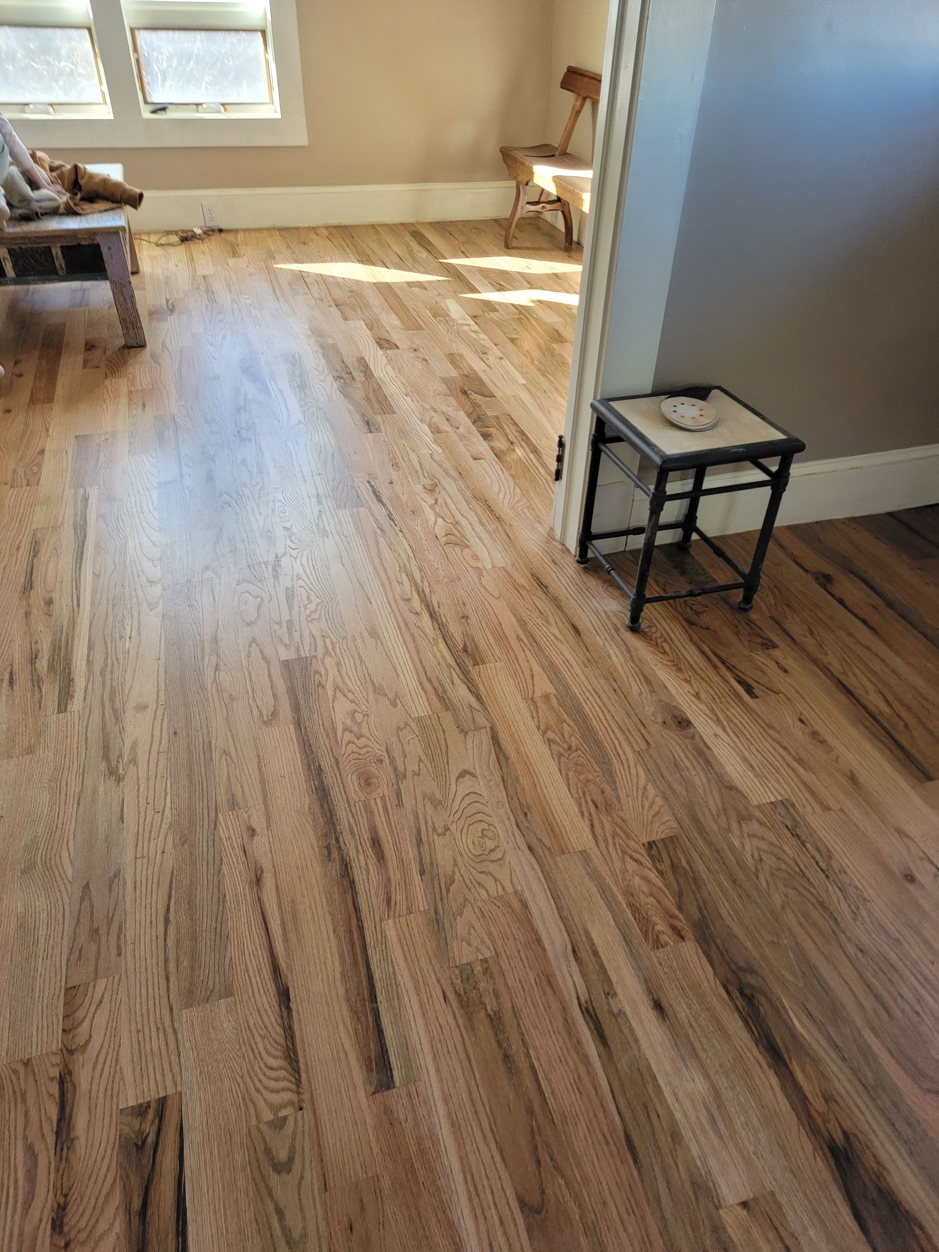Empty room with light wood flooring, small side table, and sunlight from the back window.