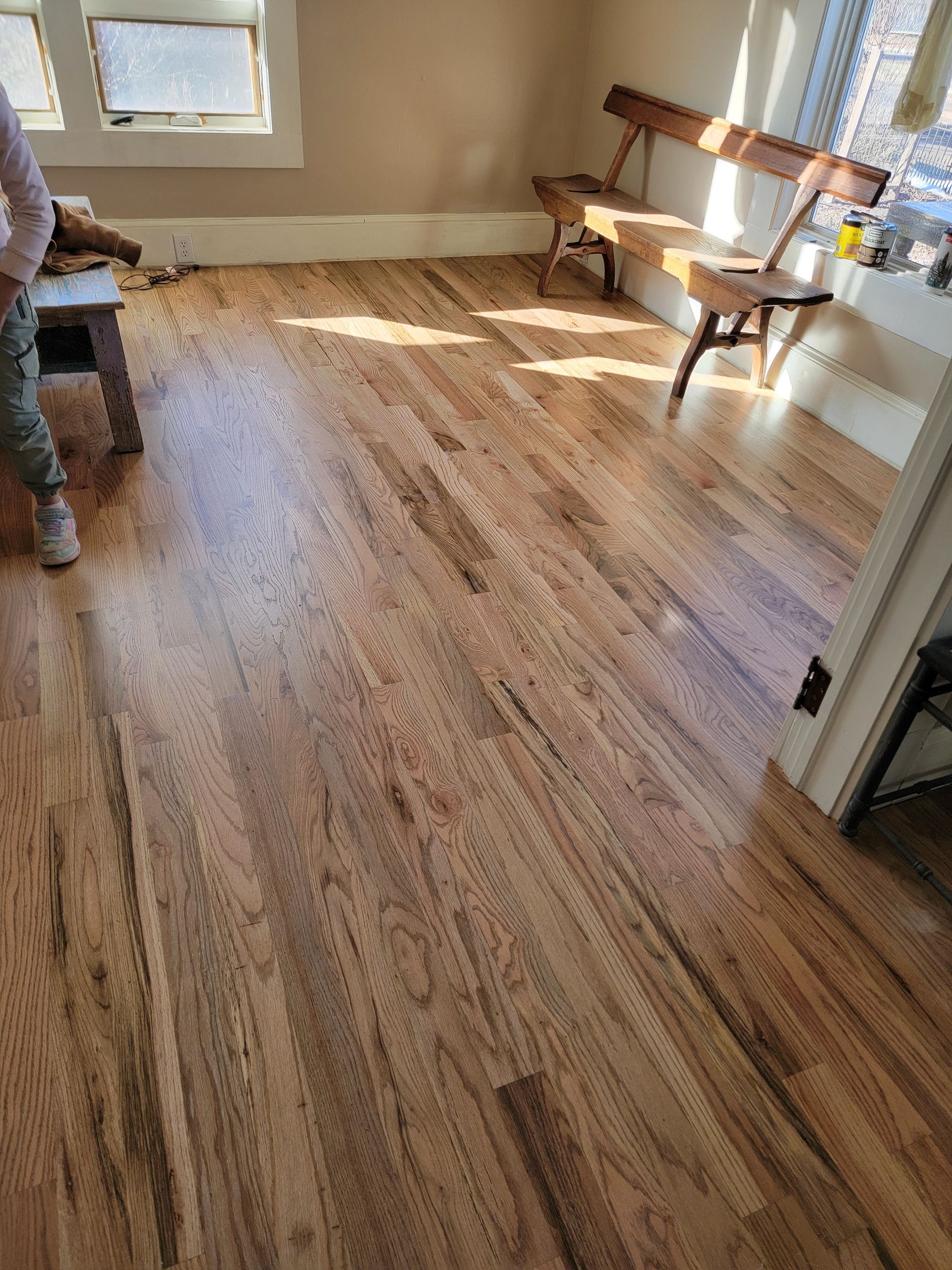 Sunlit room with wood-look flooring, window bench, and chair near the wall