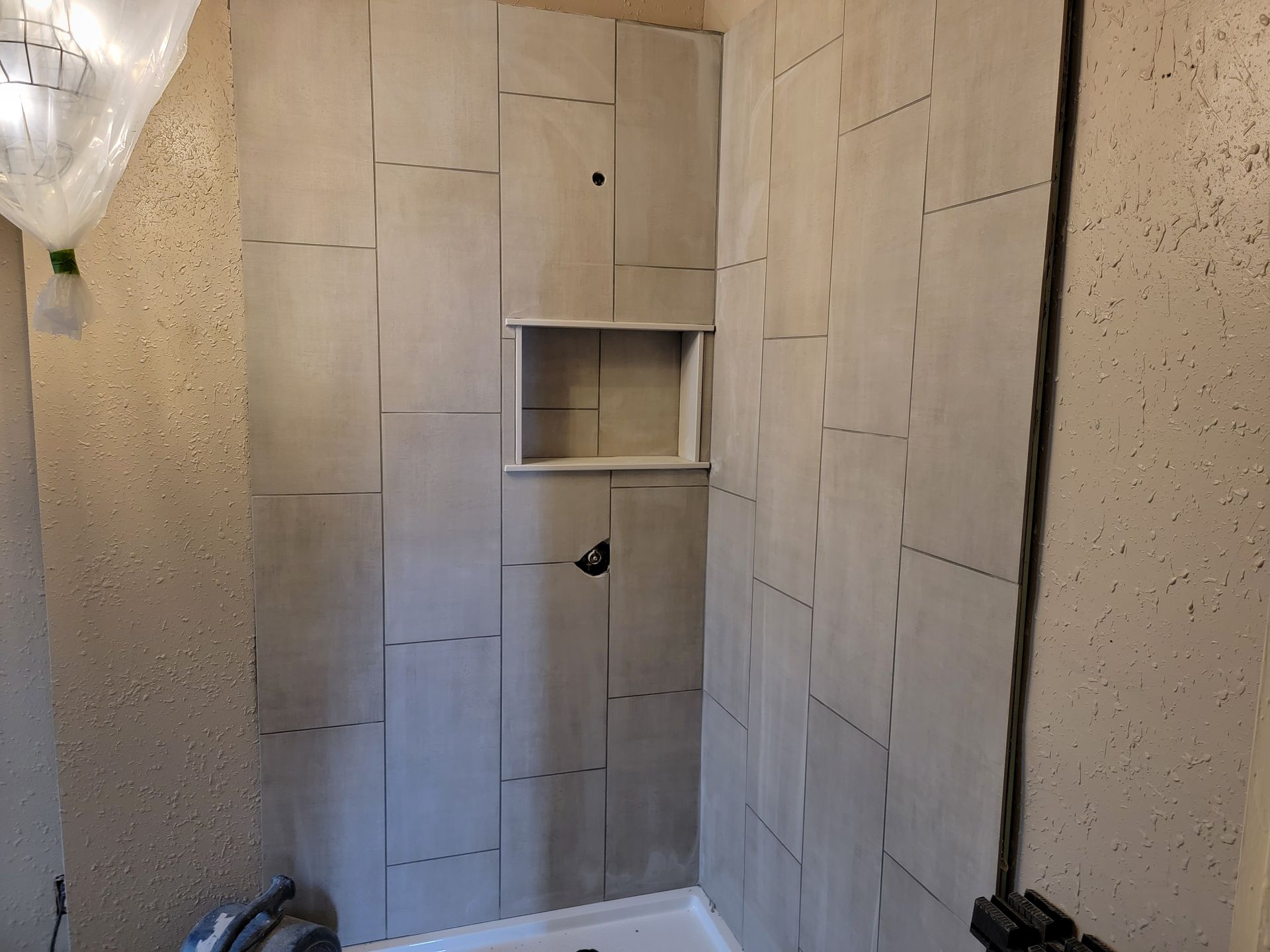 Tiled shower stall with built-in niche and shower head in a small bathroom.