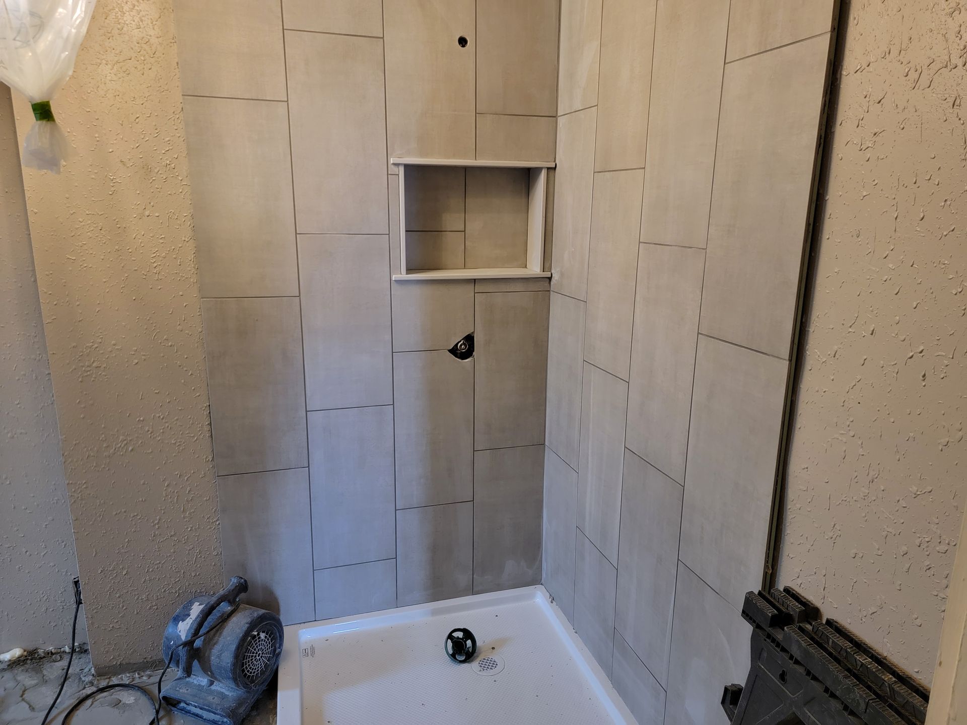 Unfinished tiled shower stall with built-in niche and plumbing on the floor