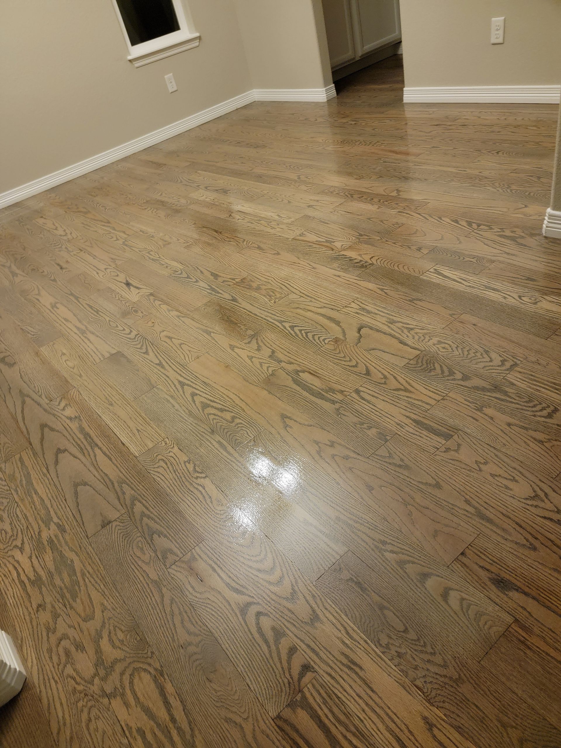 Empty hardwood-floored room with beige walls and white baseboards, viewed from a low angle.
