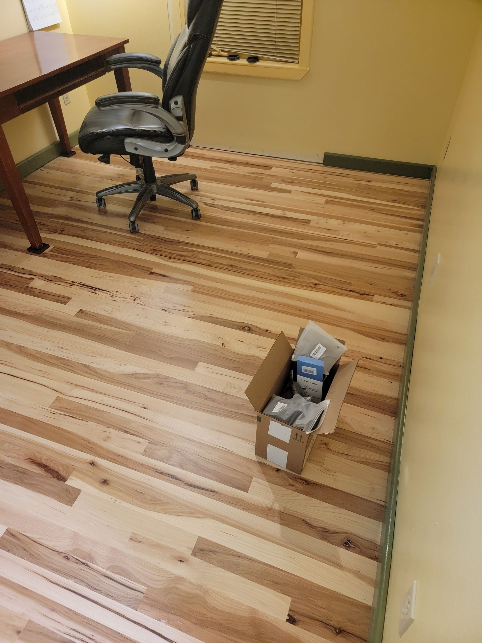 Office floor with an office chair and desk; a small open cardboard box sits on the carpet.