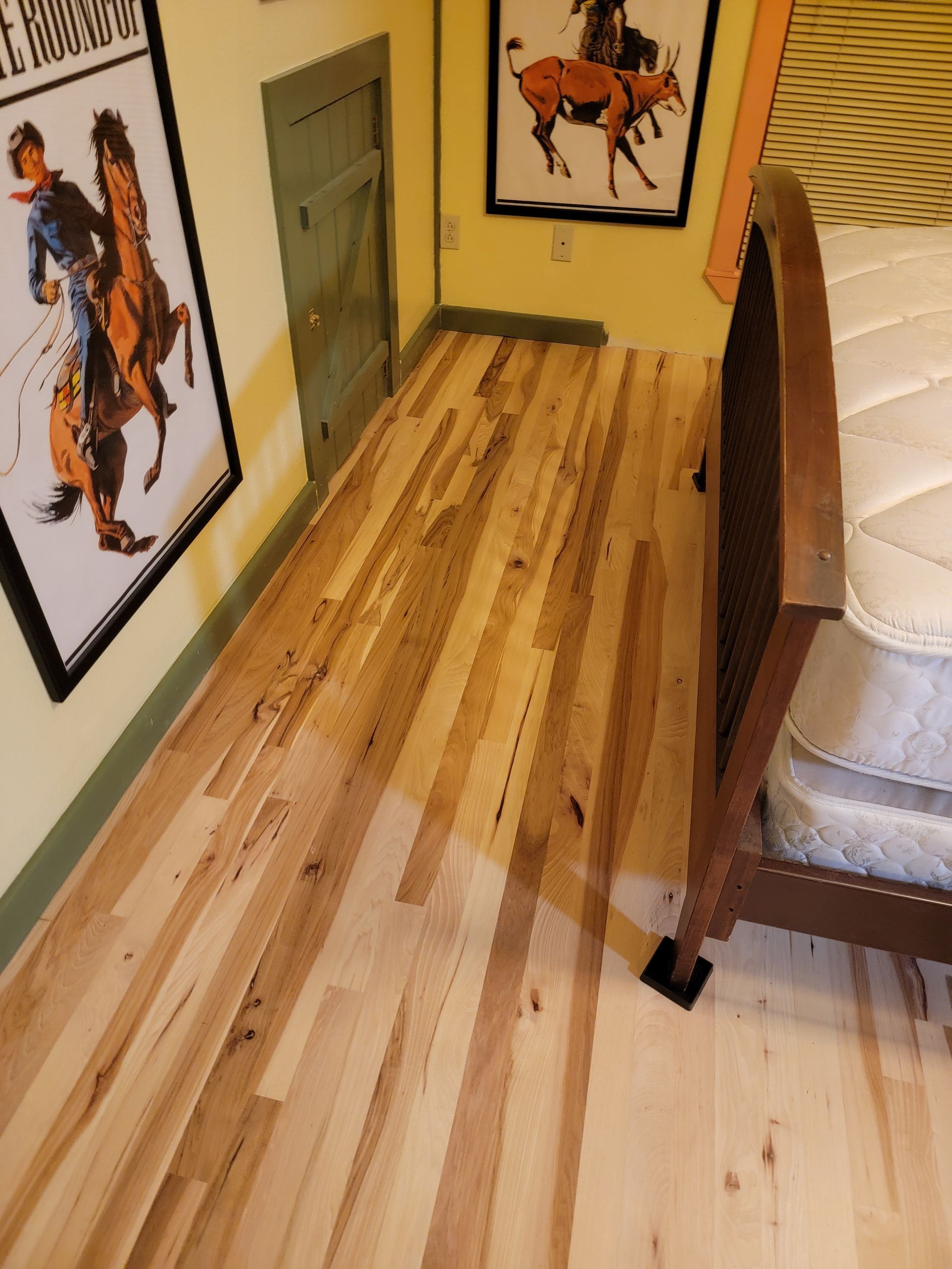 Narrow hallway with striped wooden floor, framed horse art, and a sofa edge on the right.