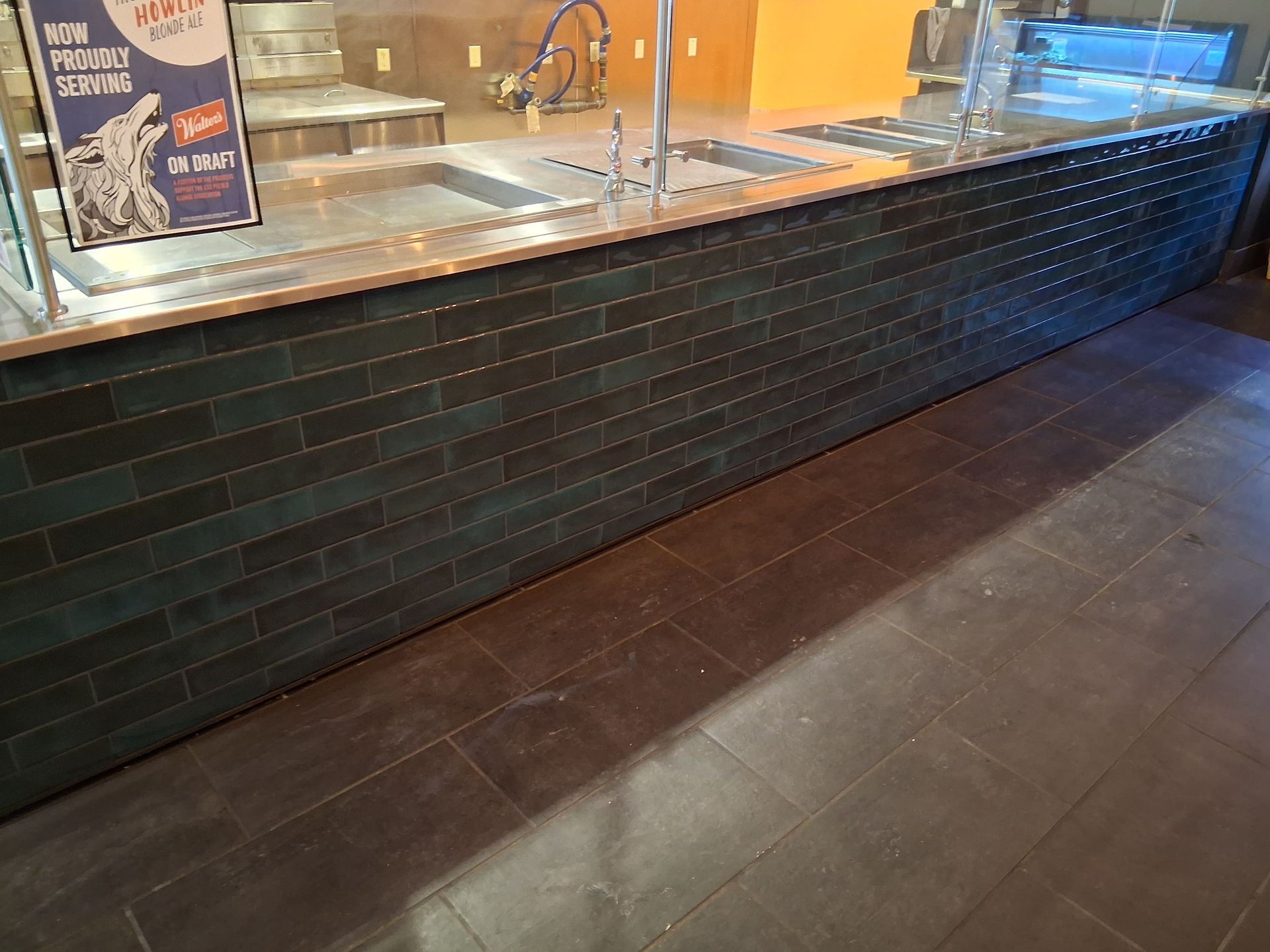 Empty restaurant counter with dark tile front and stainless steel prep area behind glass.