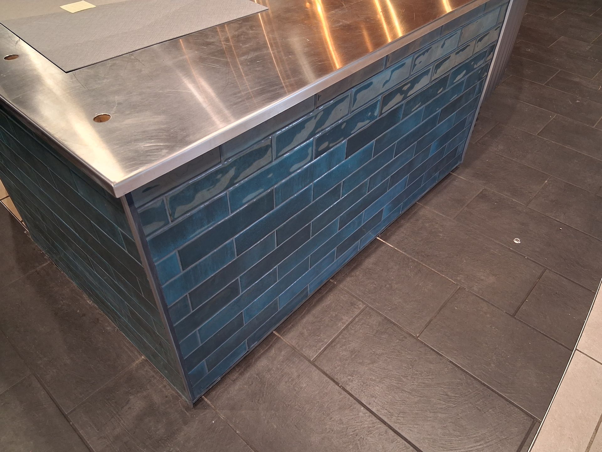 Blue tiled kiosk with a metal countertop on a dark tiled floor
