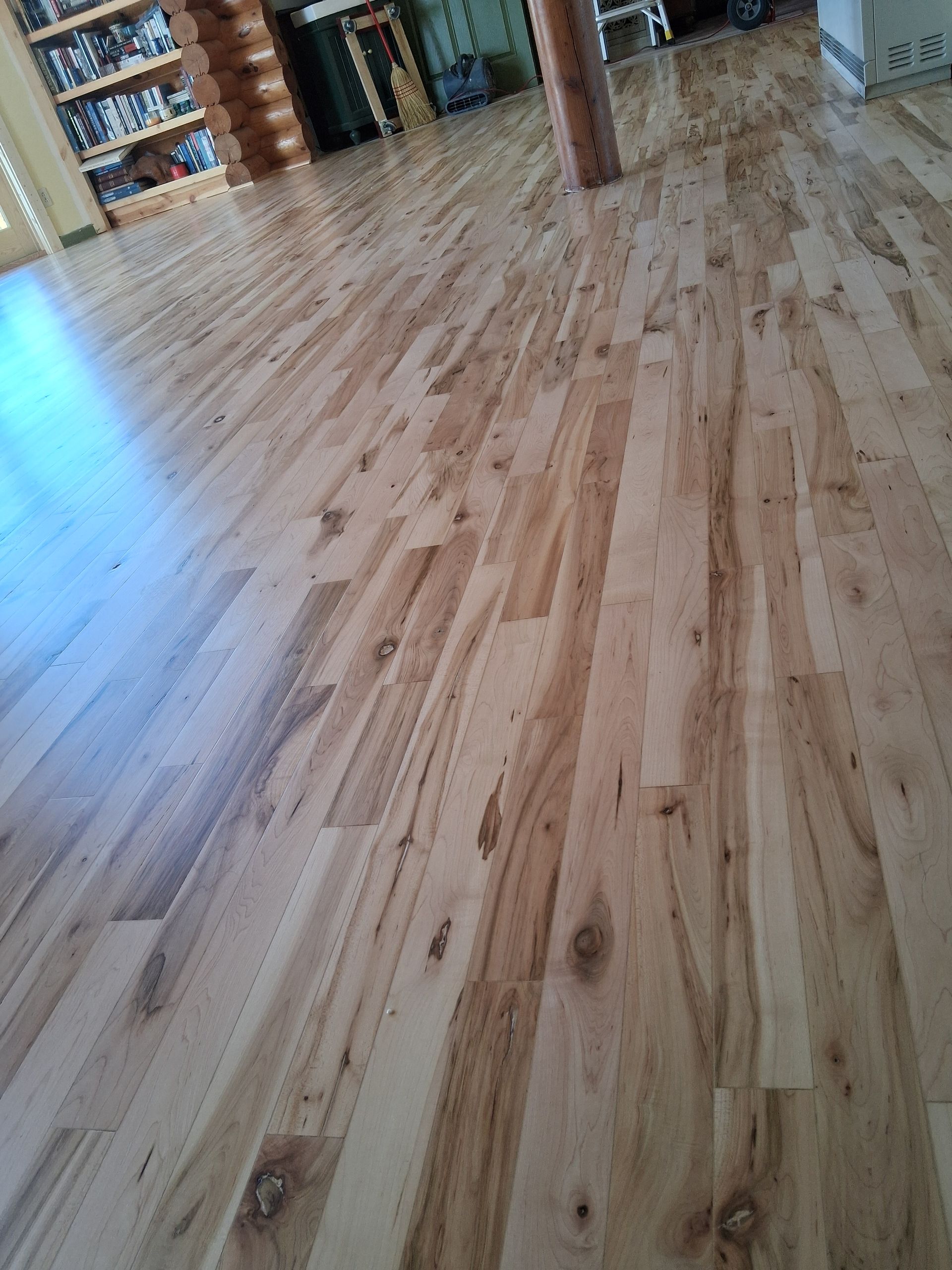 Wooden floor in an indoor room with bookshelves and a support column visible in the background.