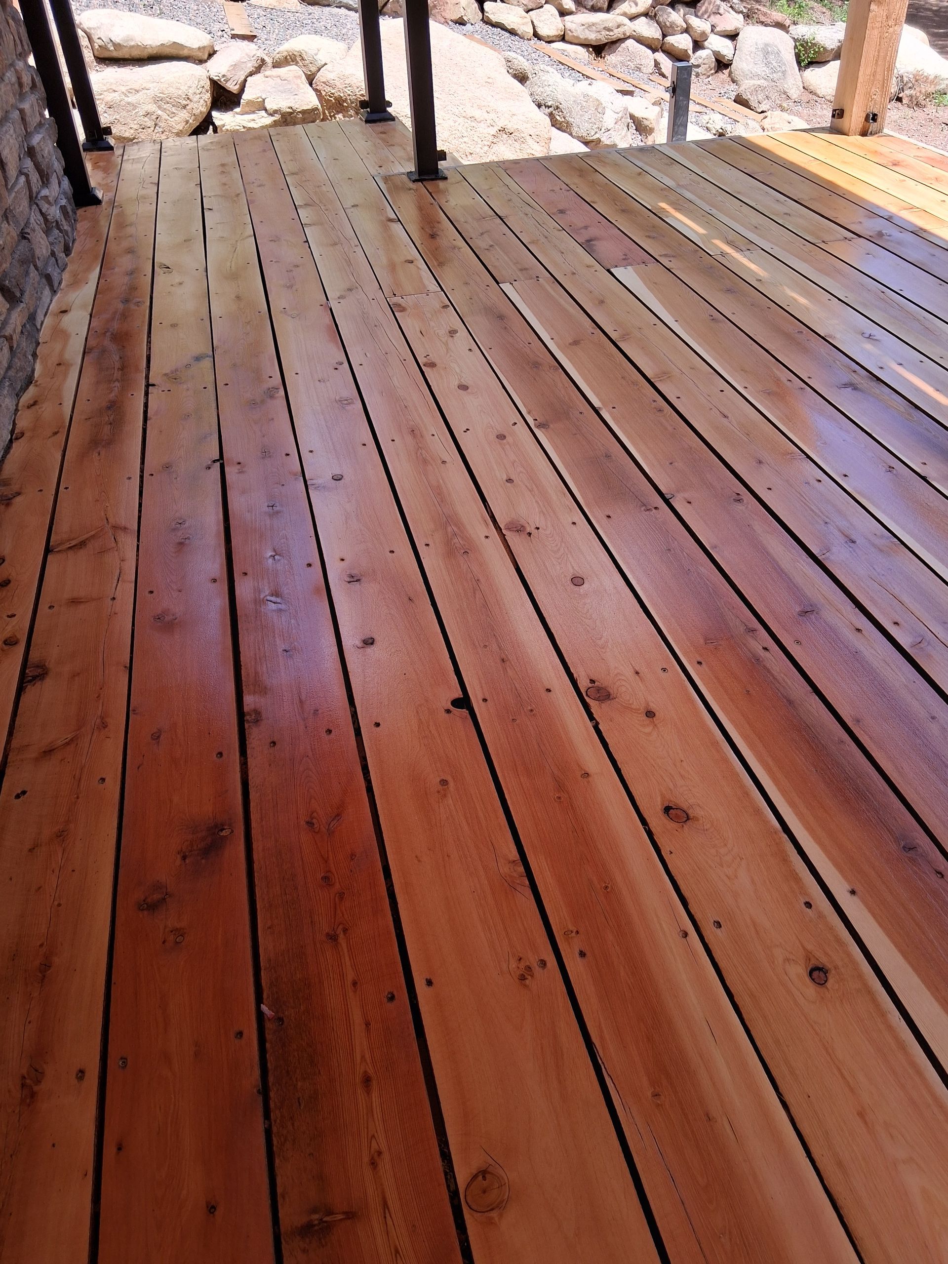 Wet reddish-brown wooden deck with stone edging and posts