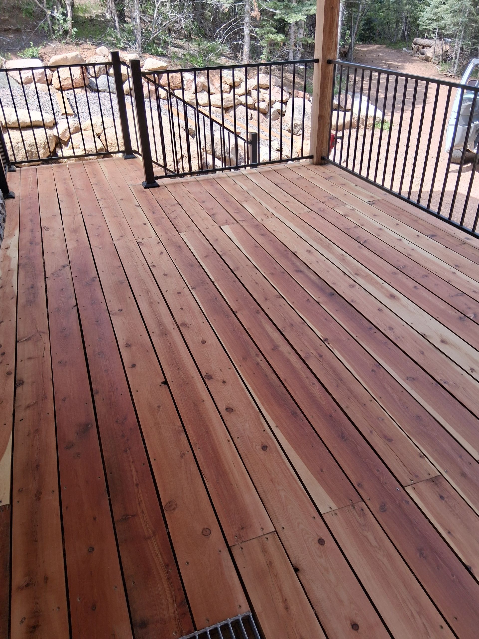 Wooden deck with black metal railing overlooking trees and a rocky outdoor area