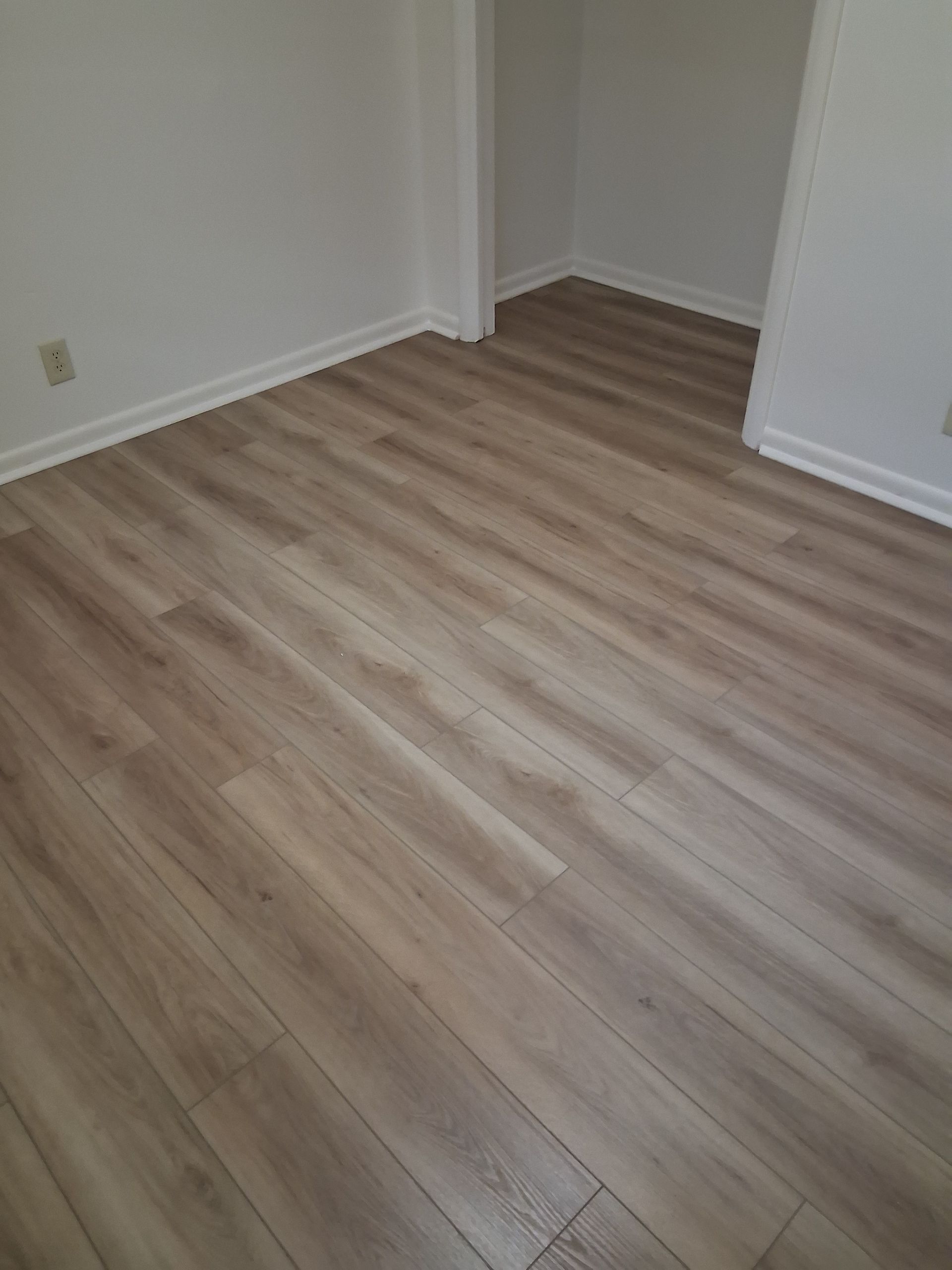 Empty room with light wood flooring and white walls, viewed from a corner.