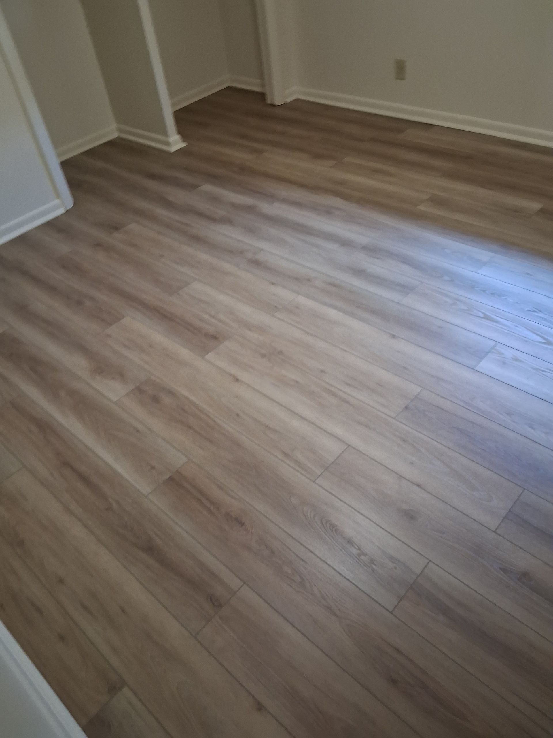 Empty room with light wood flooring and white walls, lit by natural light.