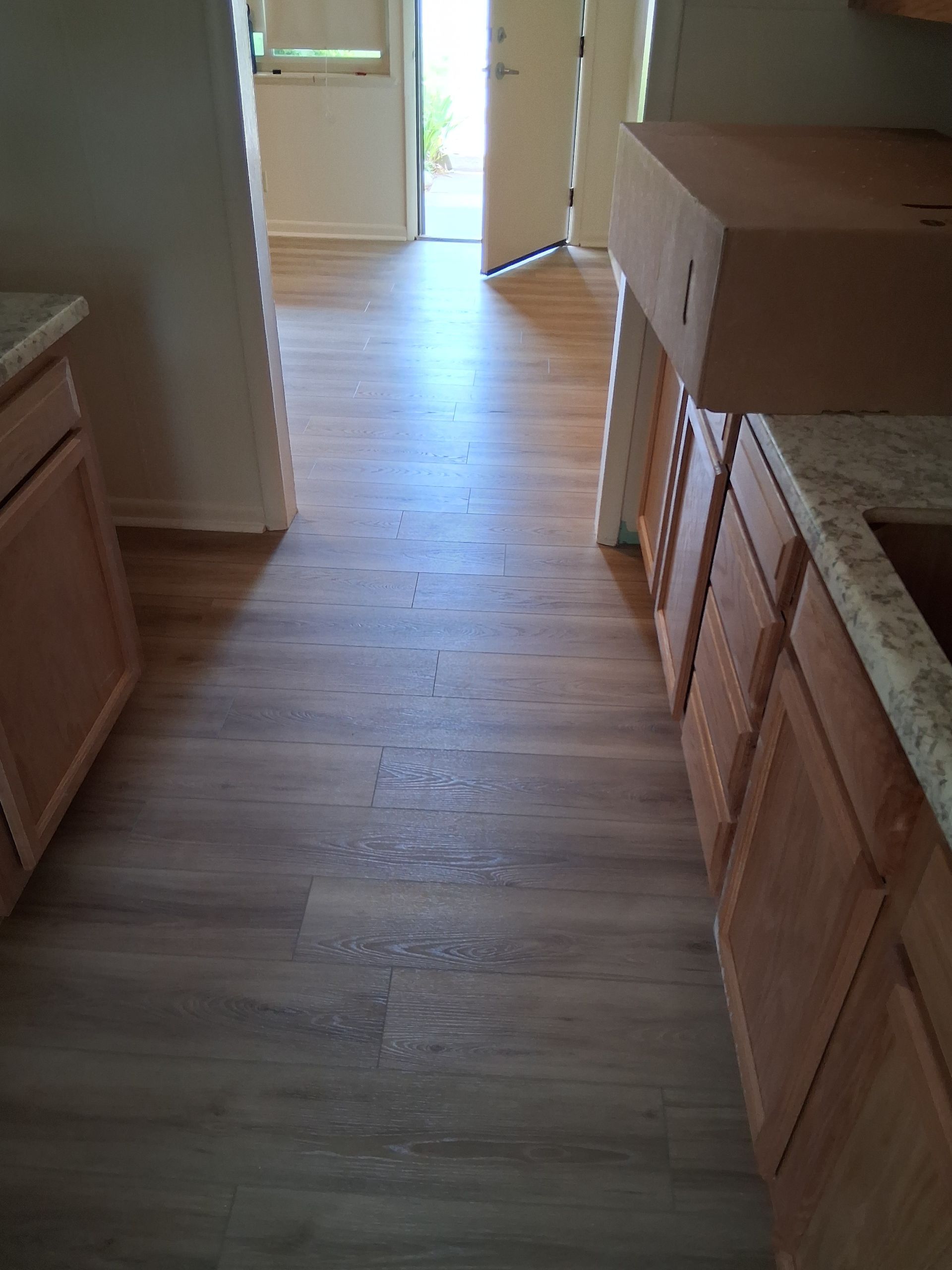 Empty hallway with light wood flooring, cabinets on the right, and a bright doorway at the end.