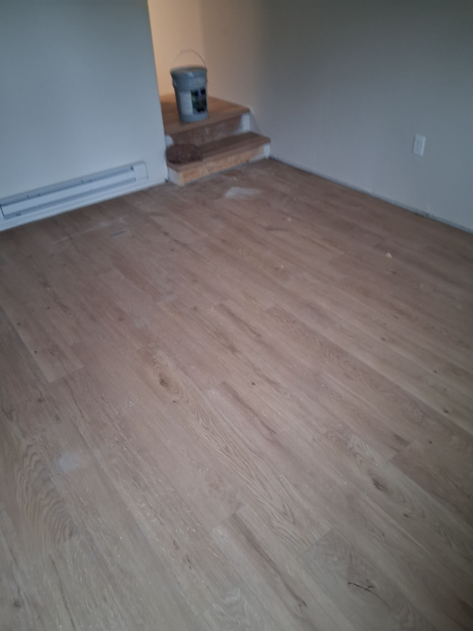 Empty room with wood flooring, baseboard heater, and a small stepped corner ledge with a bucket.