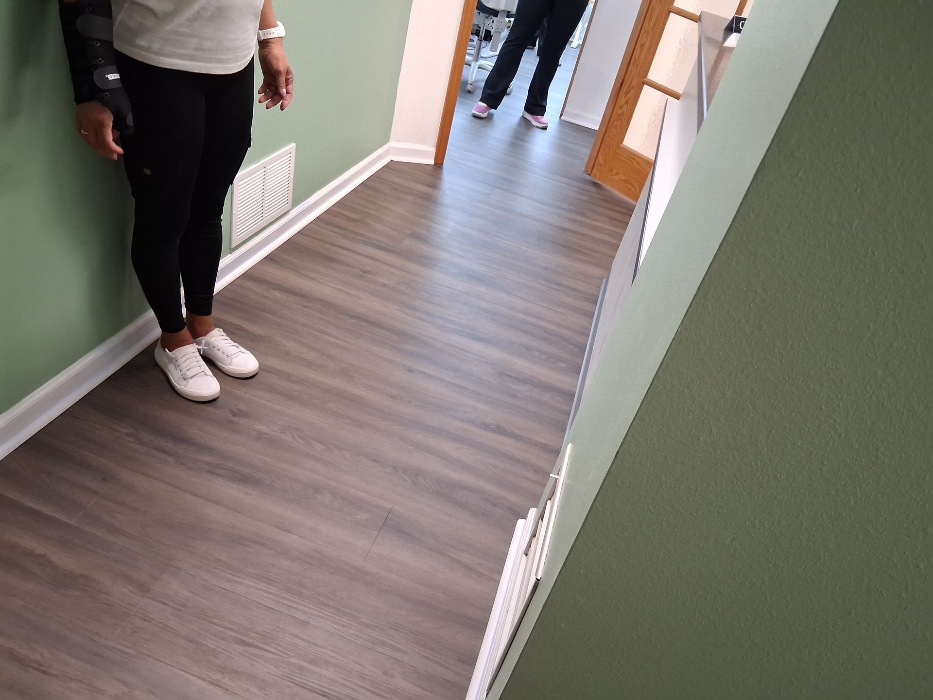 Hallway with wood-look flooring; two people stand near open doors and a radiator on the wall.
