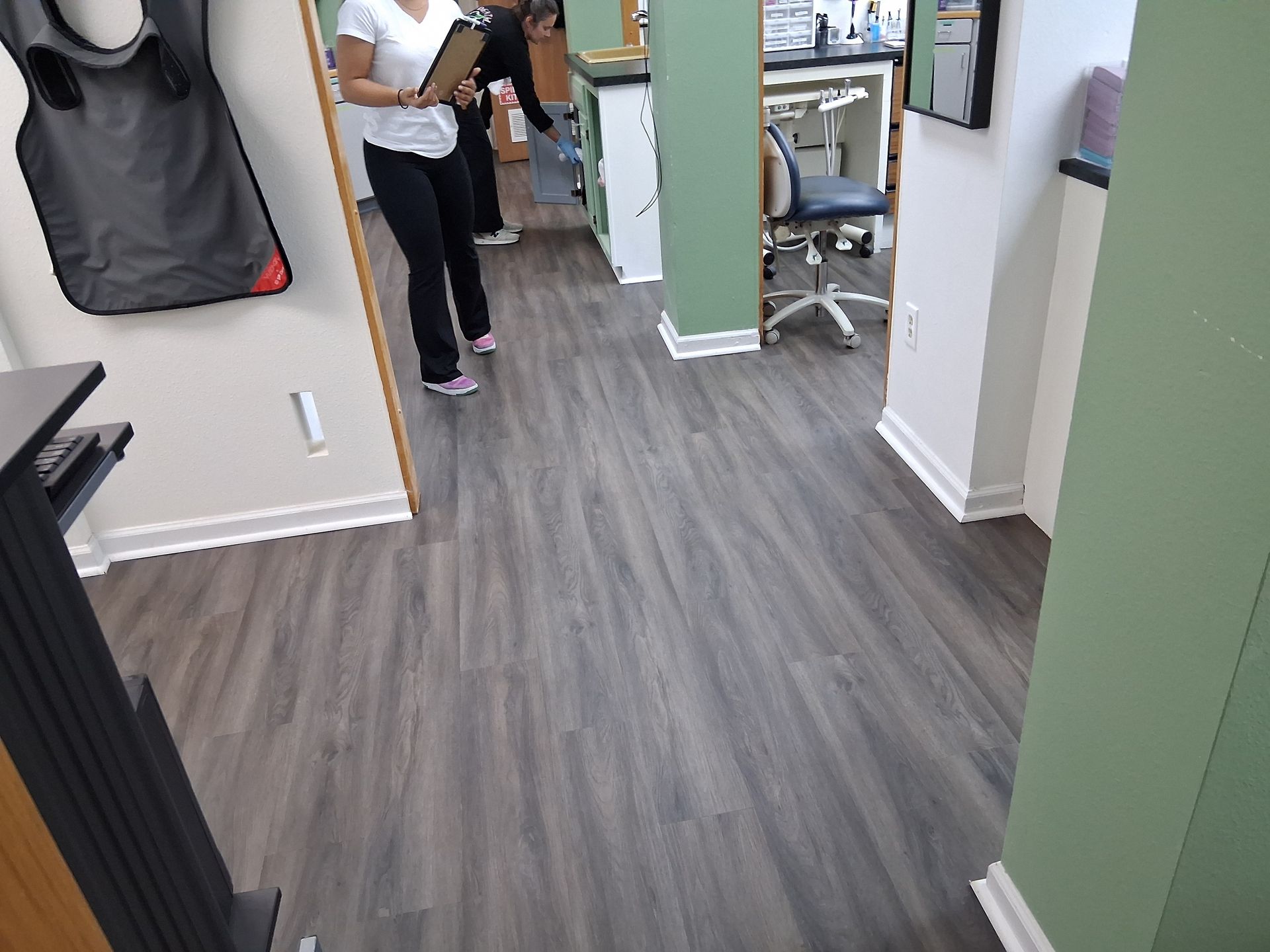Person standing in a hallway near desks, with gray flooring and green walls.