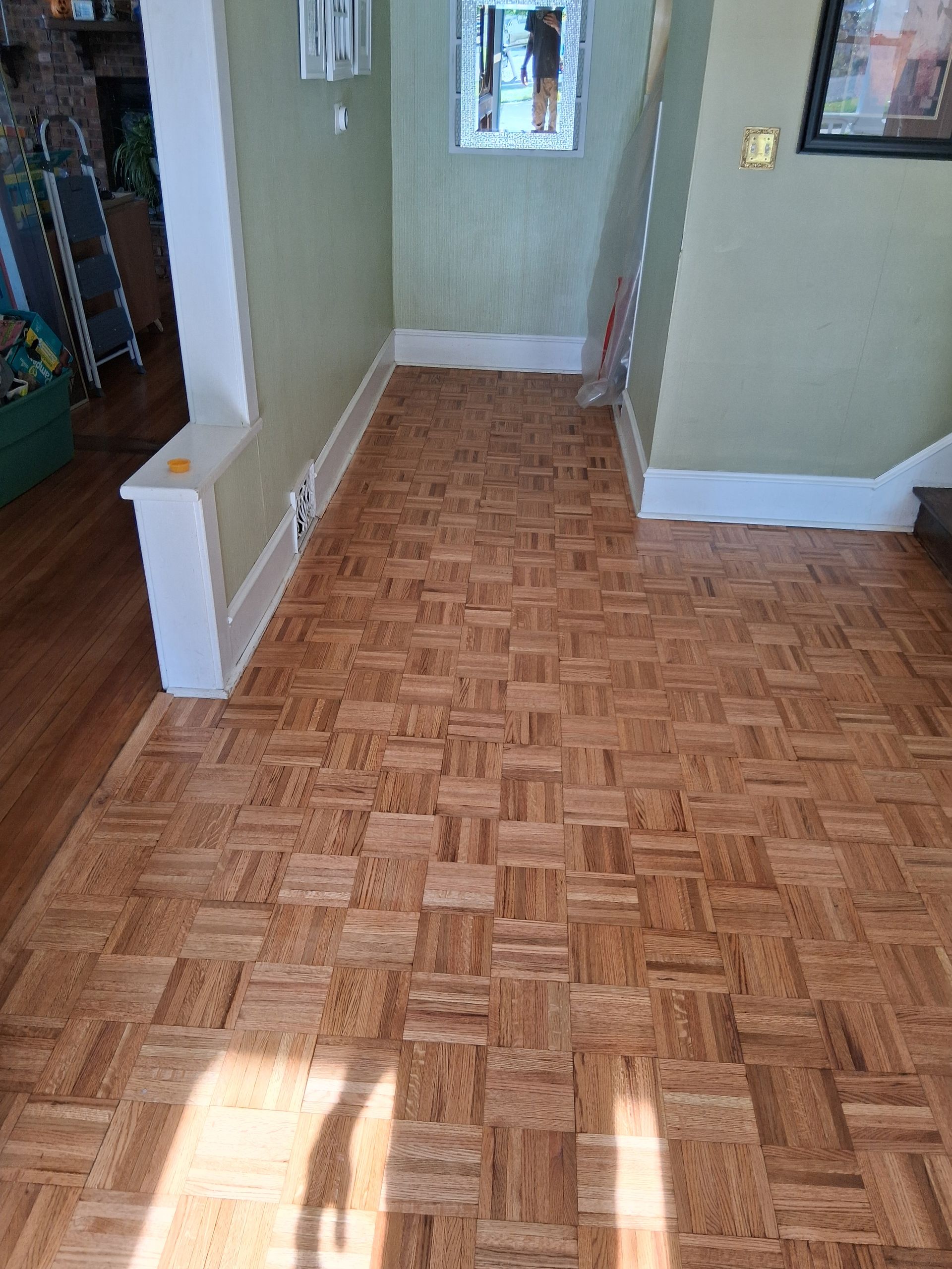 Empty hallway with parquet floor, green walls, and sunlight streaming through a window.