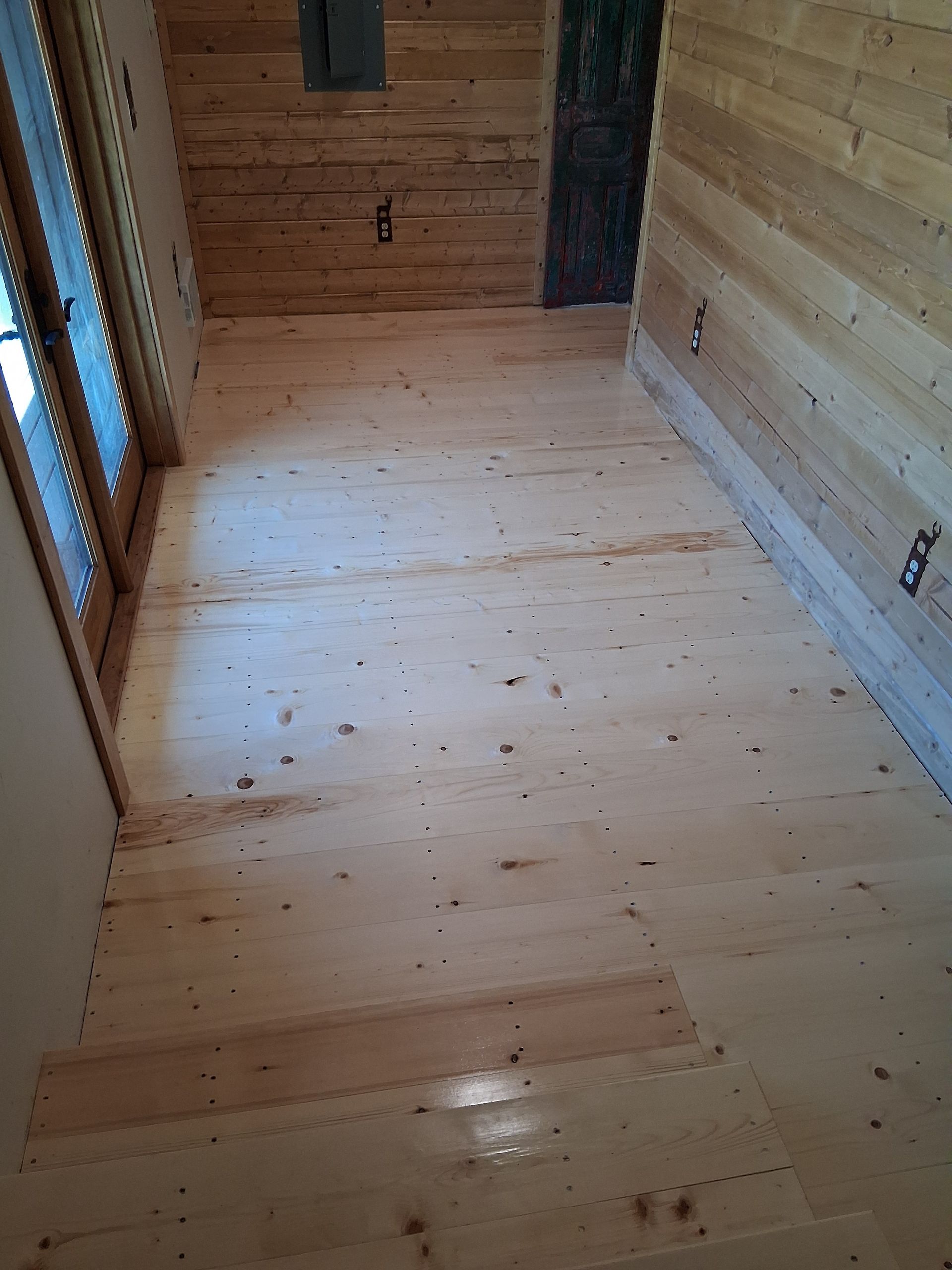 Narrow unfinished wooden room with plank floor, walls, and window openings