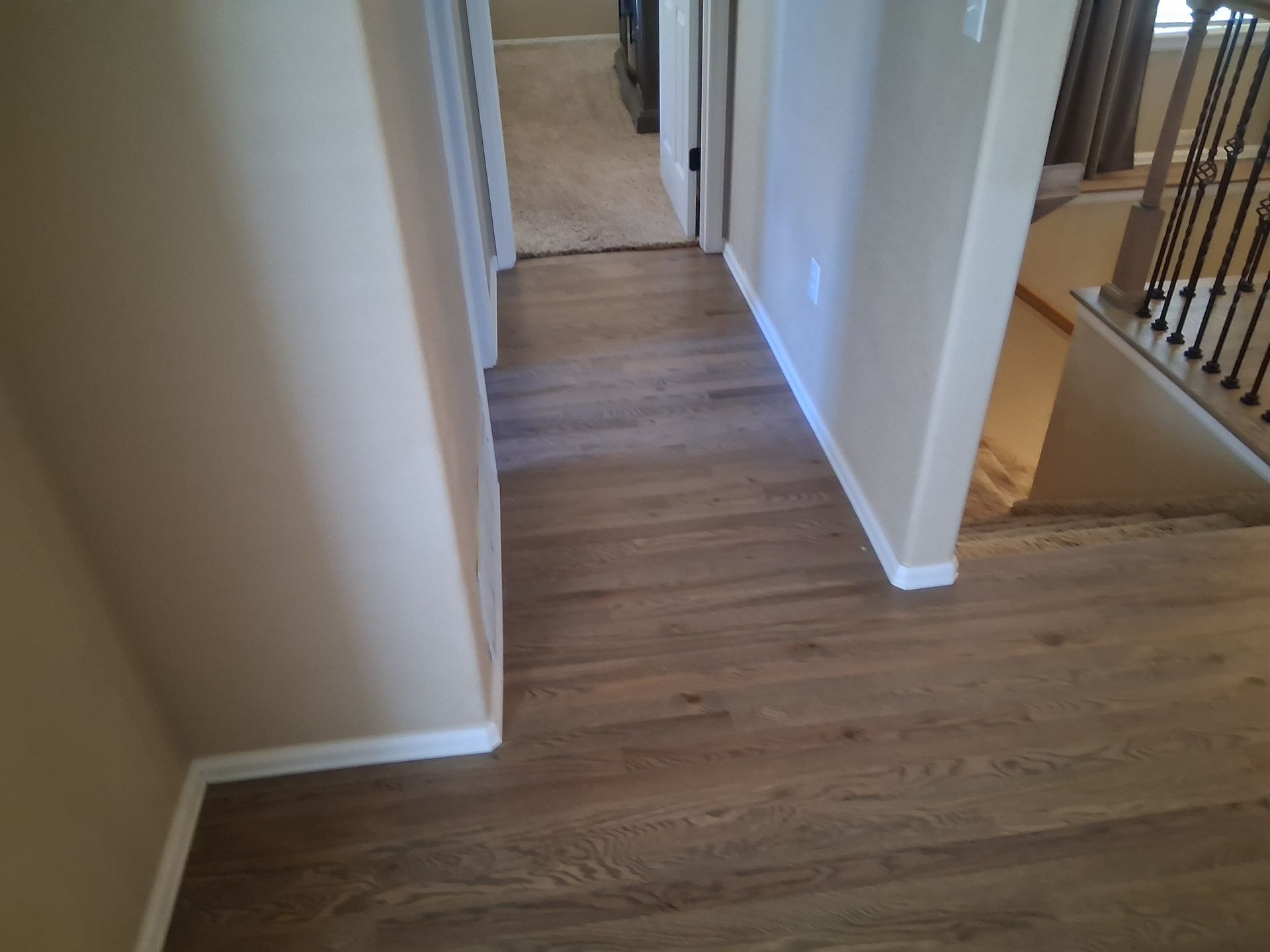 Wood-floored hallway with white walls and doorway leading to stairs on the right