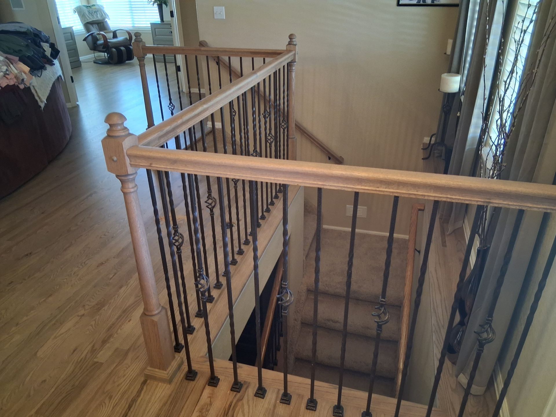 Wooden staircase with black iron balusters overlooking a hardwood hallway and entryway below