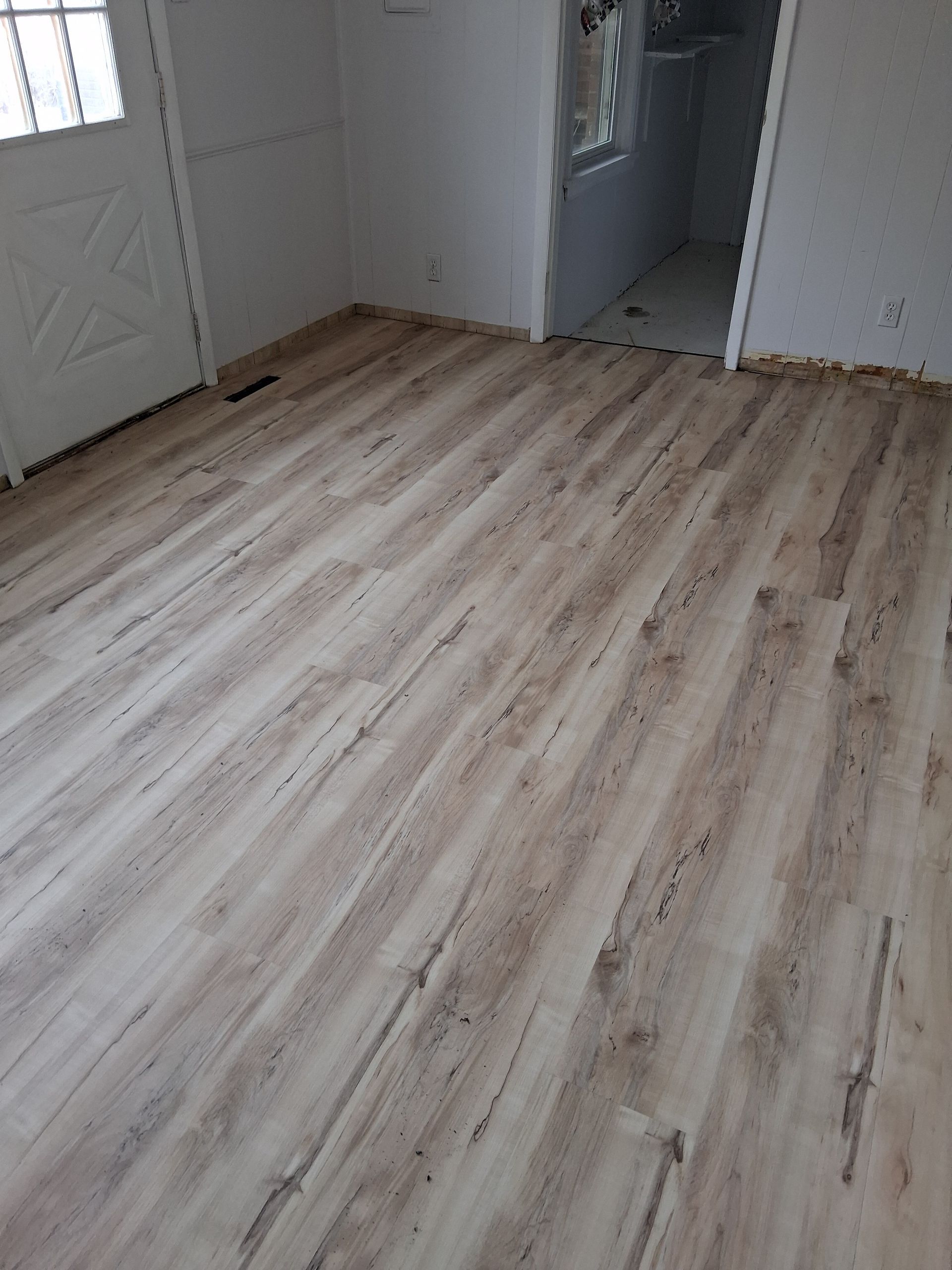 Empty room with light wood-look flooring and white walls, viewed toward a doorway.