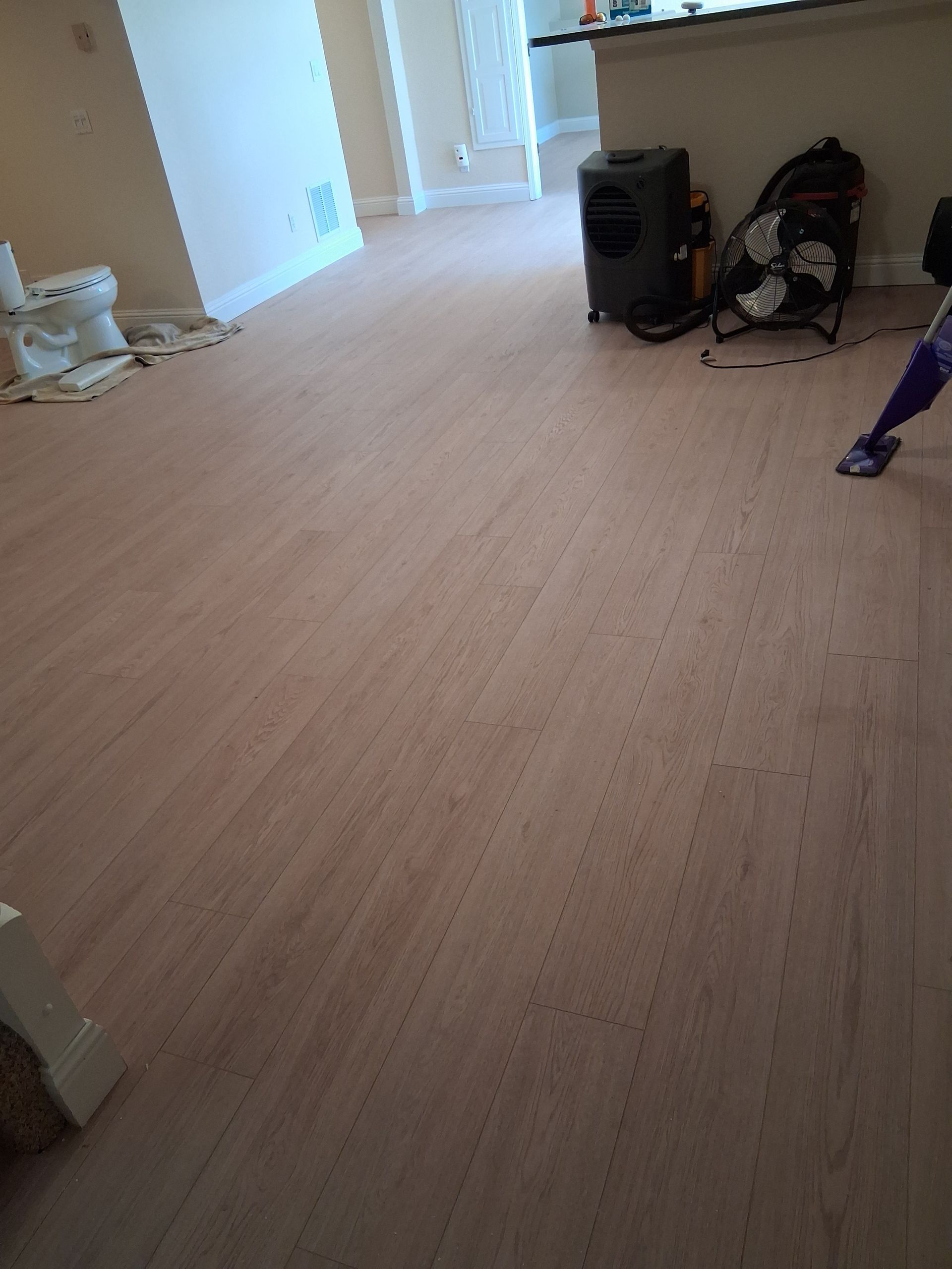 Empty room with light wood flooring, a few items near the walls, and a hallway in the background