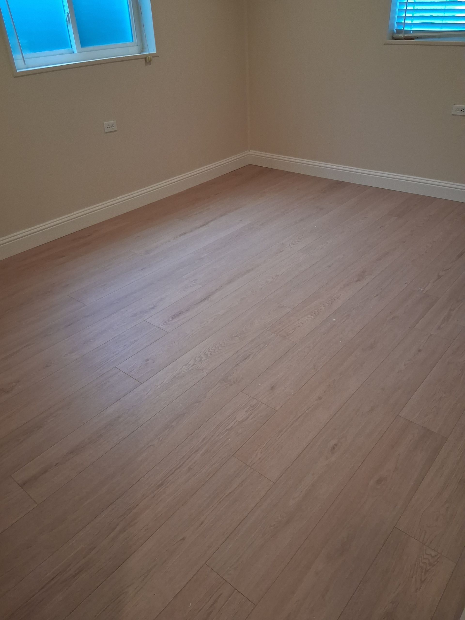 Empty beige room with light wood flooring and two blue-tinted windows