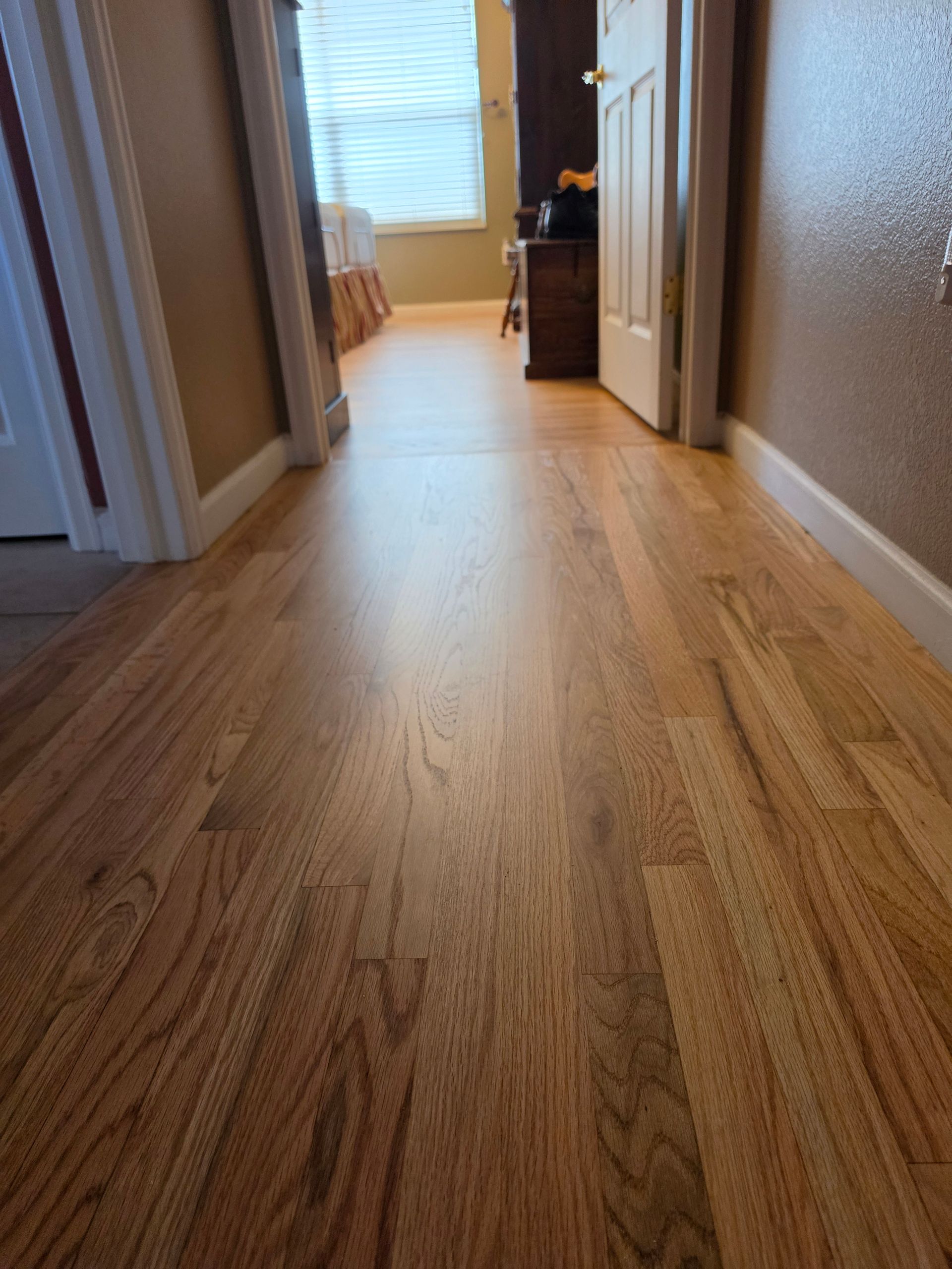 Wooden hallway with light hardwood floors leading to a bright room at the end