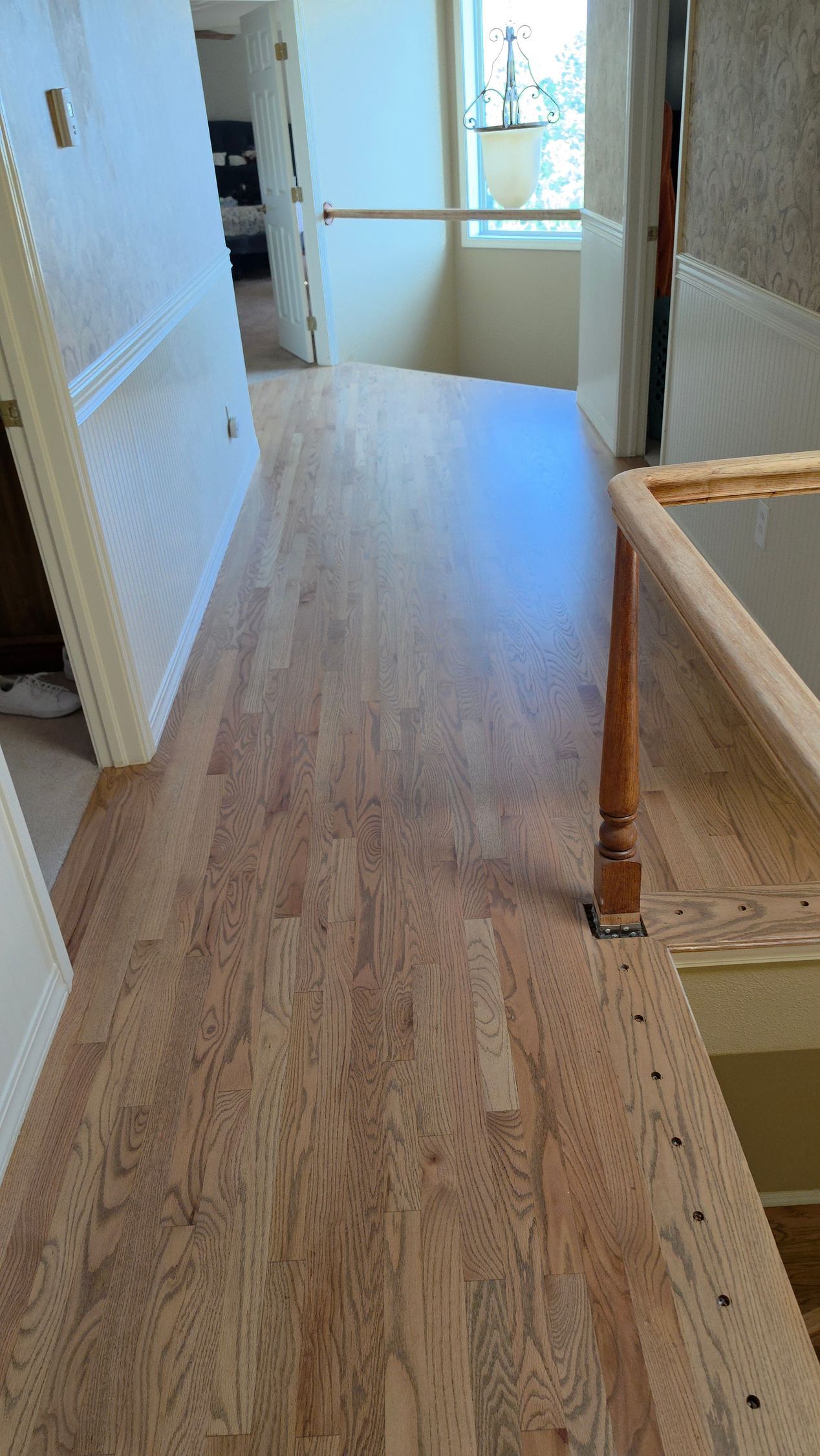 Narrow hallway with light wood floor, white walls, and a staircase railing on the right.