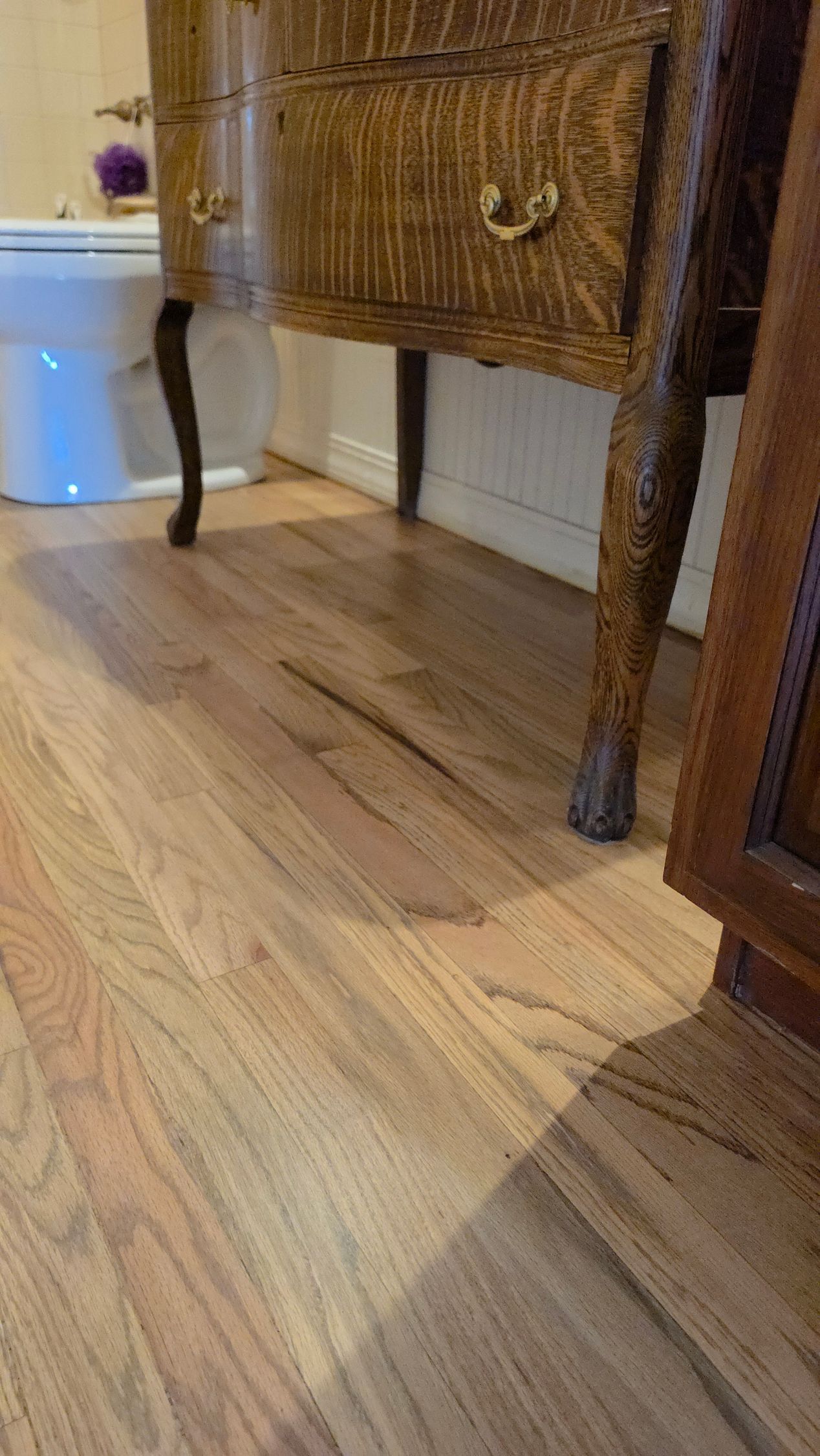 Wooden side table with carved legs on a hardwood floor beside a wall outlet and another cabinet