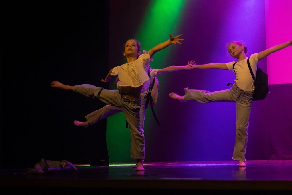 Twee dansers met gestrekte armen en benen in paars en groen podiumlicht