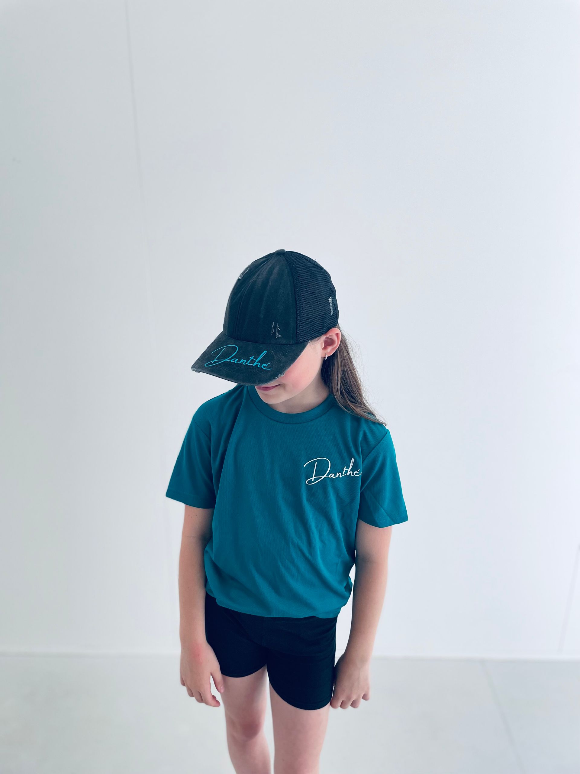 Een meisje in een groenblauw Danthé-sportshirt en een pet