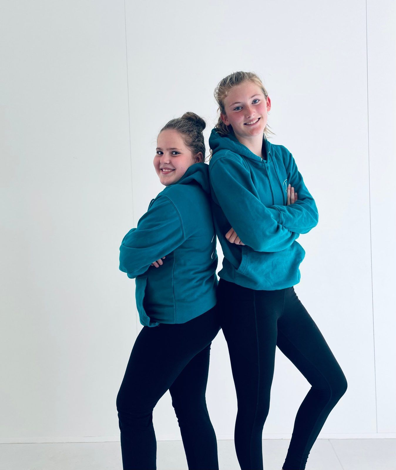 Twee lachende leerlingen in groenblauwe Danthé-hoodies staan rug aan rug