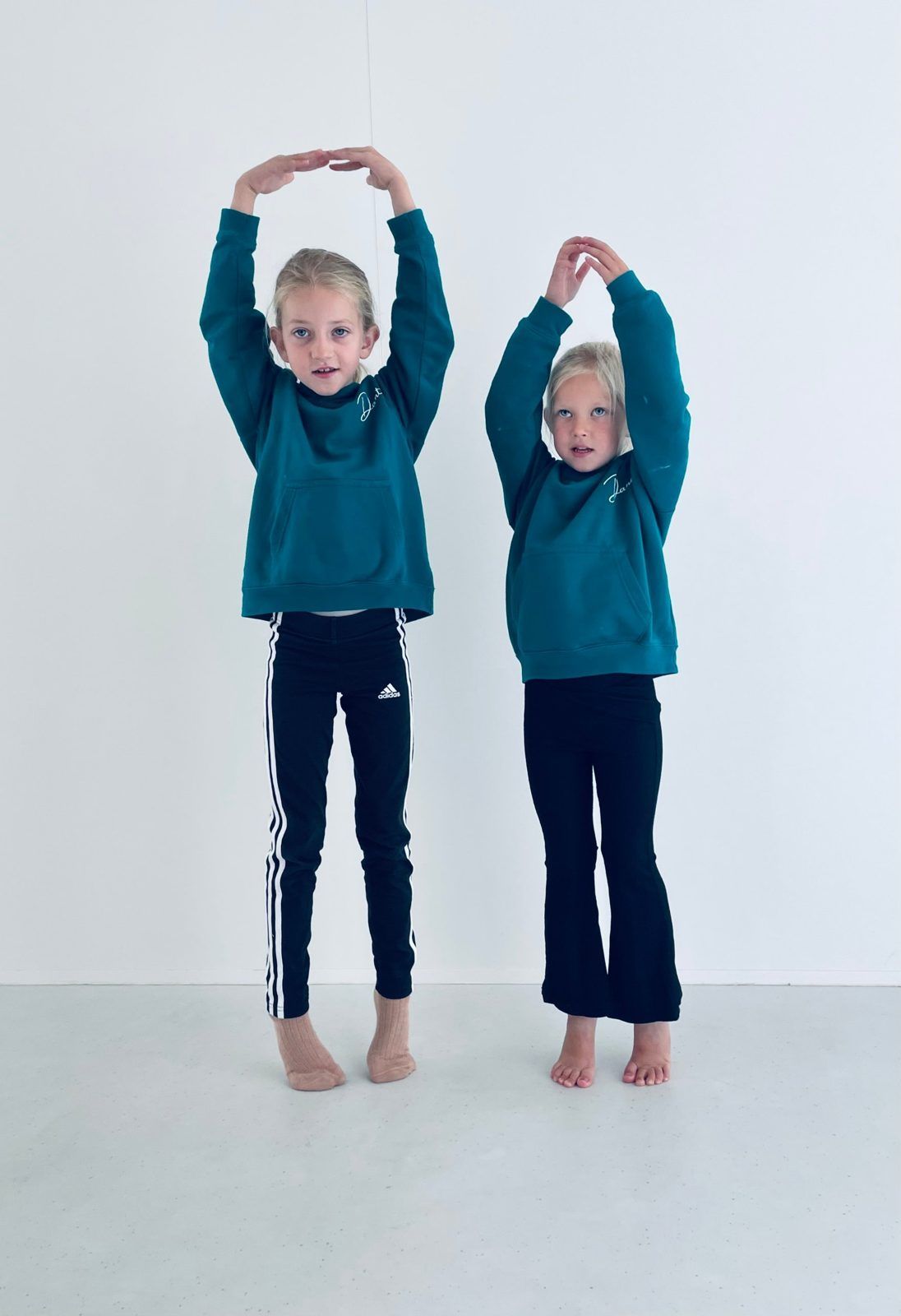 Twee jonge dansers in groenblauwe Danthé-hoodies met de armen in een boog boven het hoofd