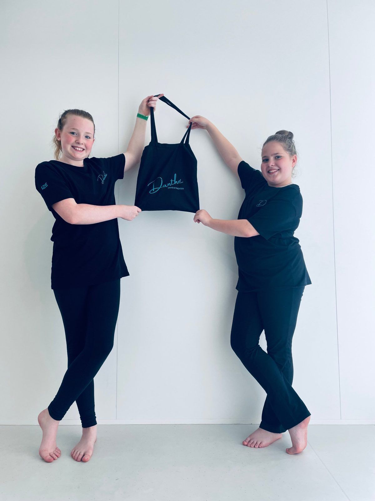 Twee leerlingen in zwarte Danthé-T-shirts houden samen een zwarte Danthé-tas omhoog