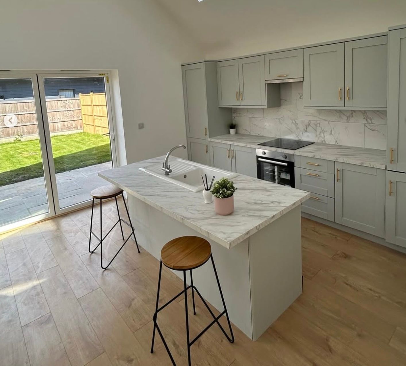 Bright modern kitchen with marble island, pale cabinets, and sliding doors to a grassy backyard.