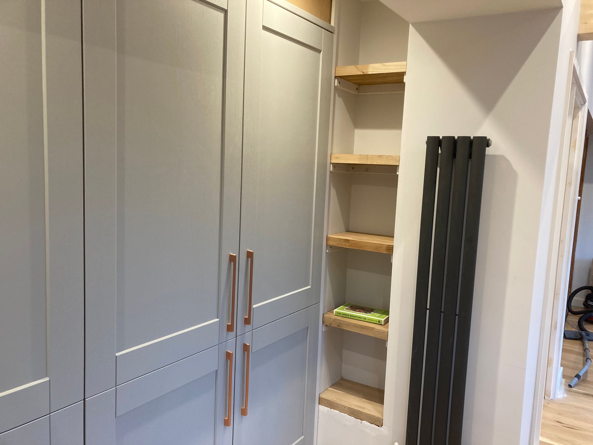 Built-in gray cabinets with copper handles beside a narrow shelving nook and radiator