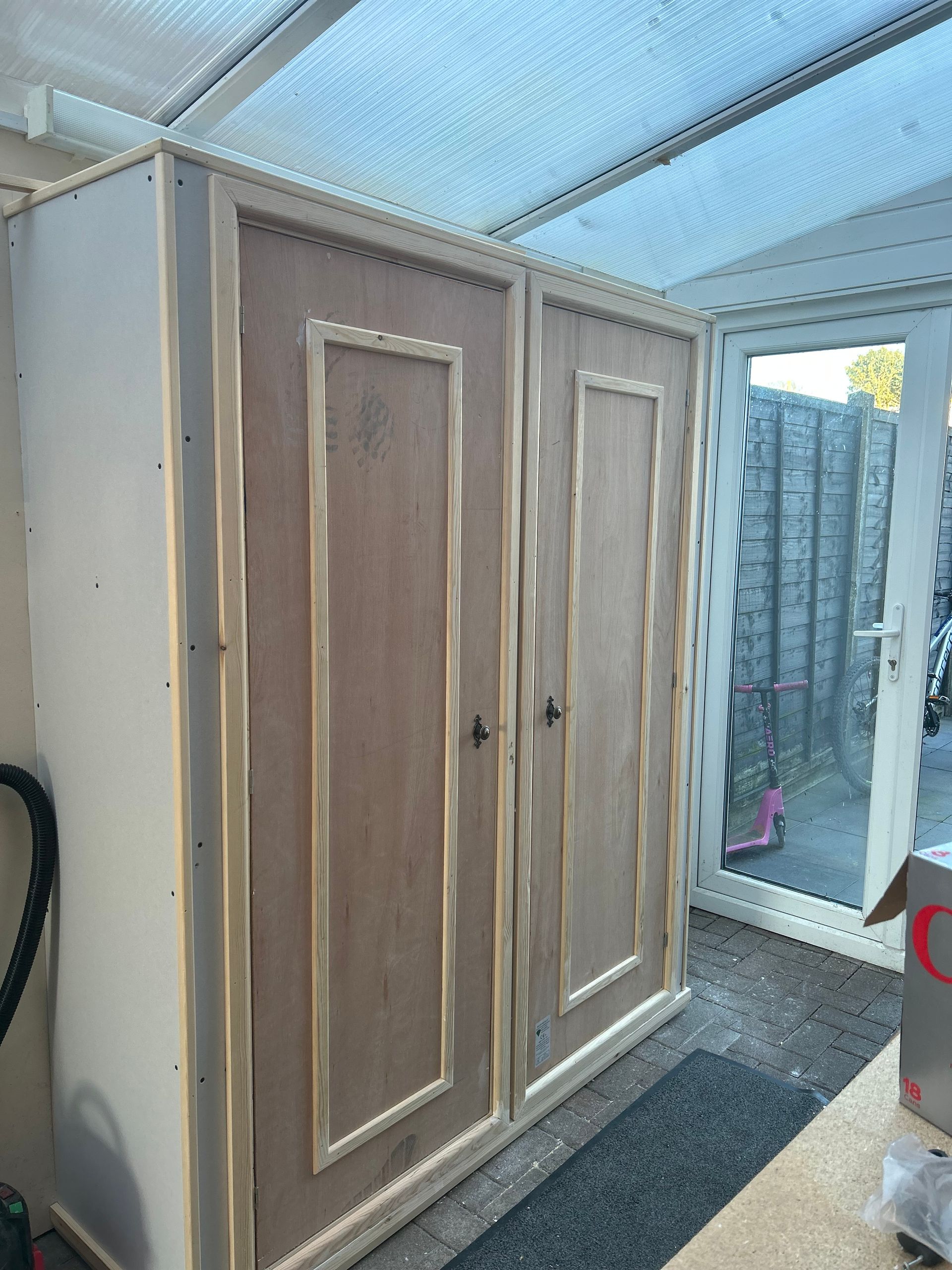 Two wooden wardrobe doors in a small indoor storage area with a translucent roof and tiled floor